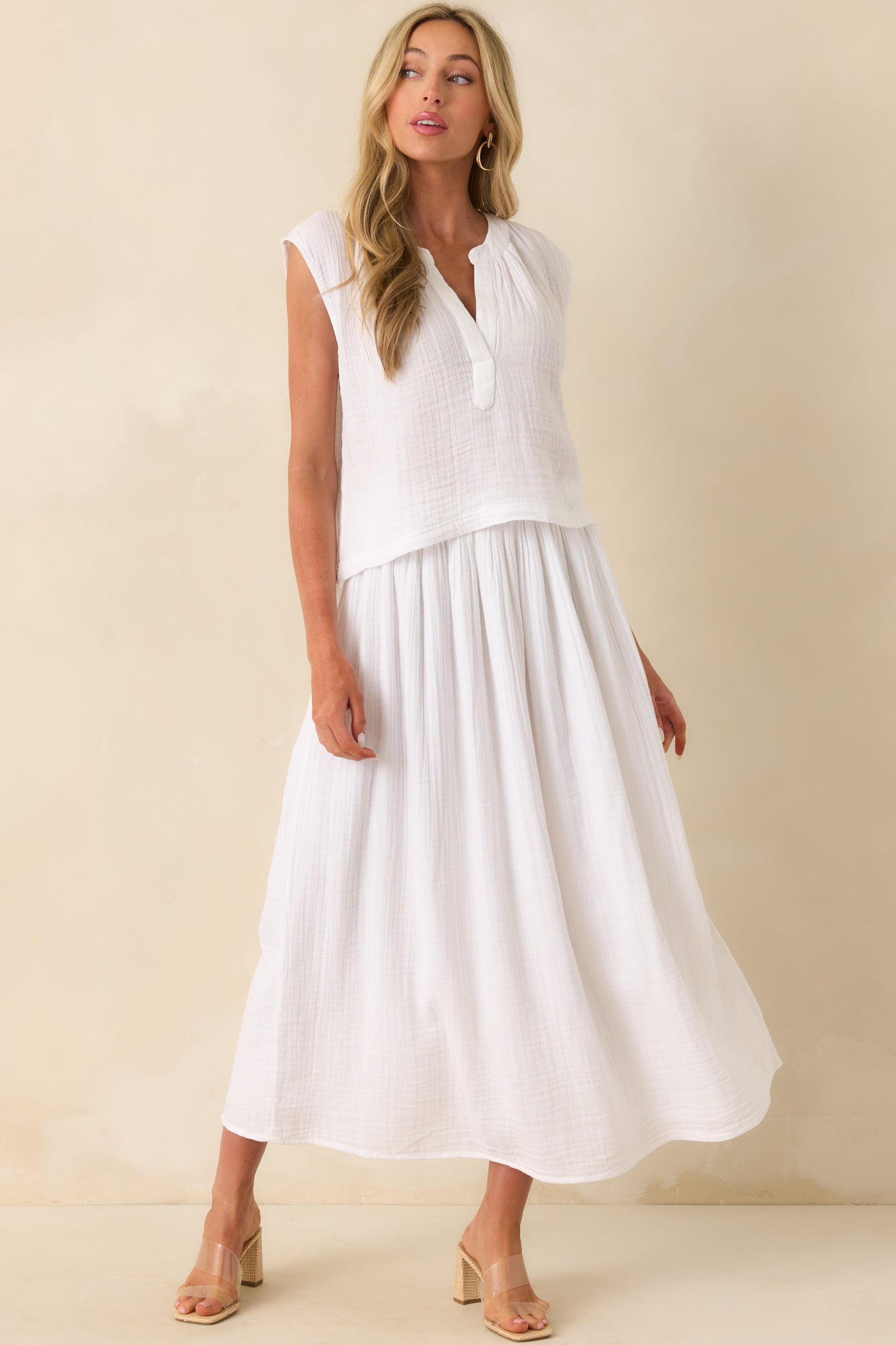 Photo of model wearing a white skirt that features a lightweight 100% cotton gauze fabric, high rise design, elastic waistband, relaxed fit, midi length, leg slit, and wearing a matching top.