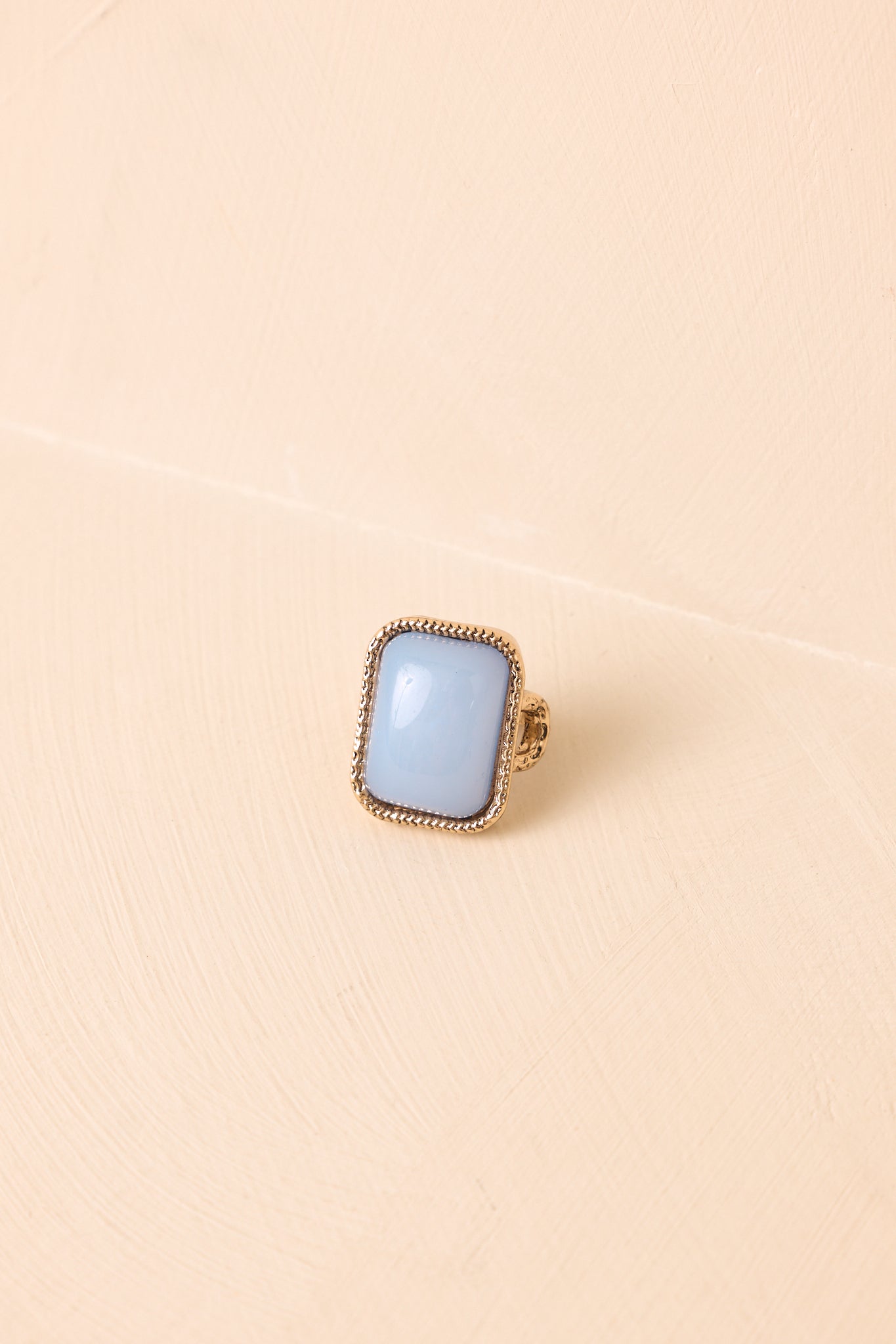 Sky blue cabochon stone ring featuring an antiqued gold-tone beaded bezel, adjustable open-back band, and vintage-inspired heirloom design against a beige background.