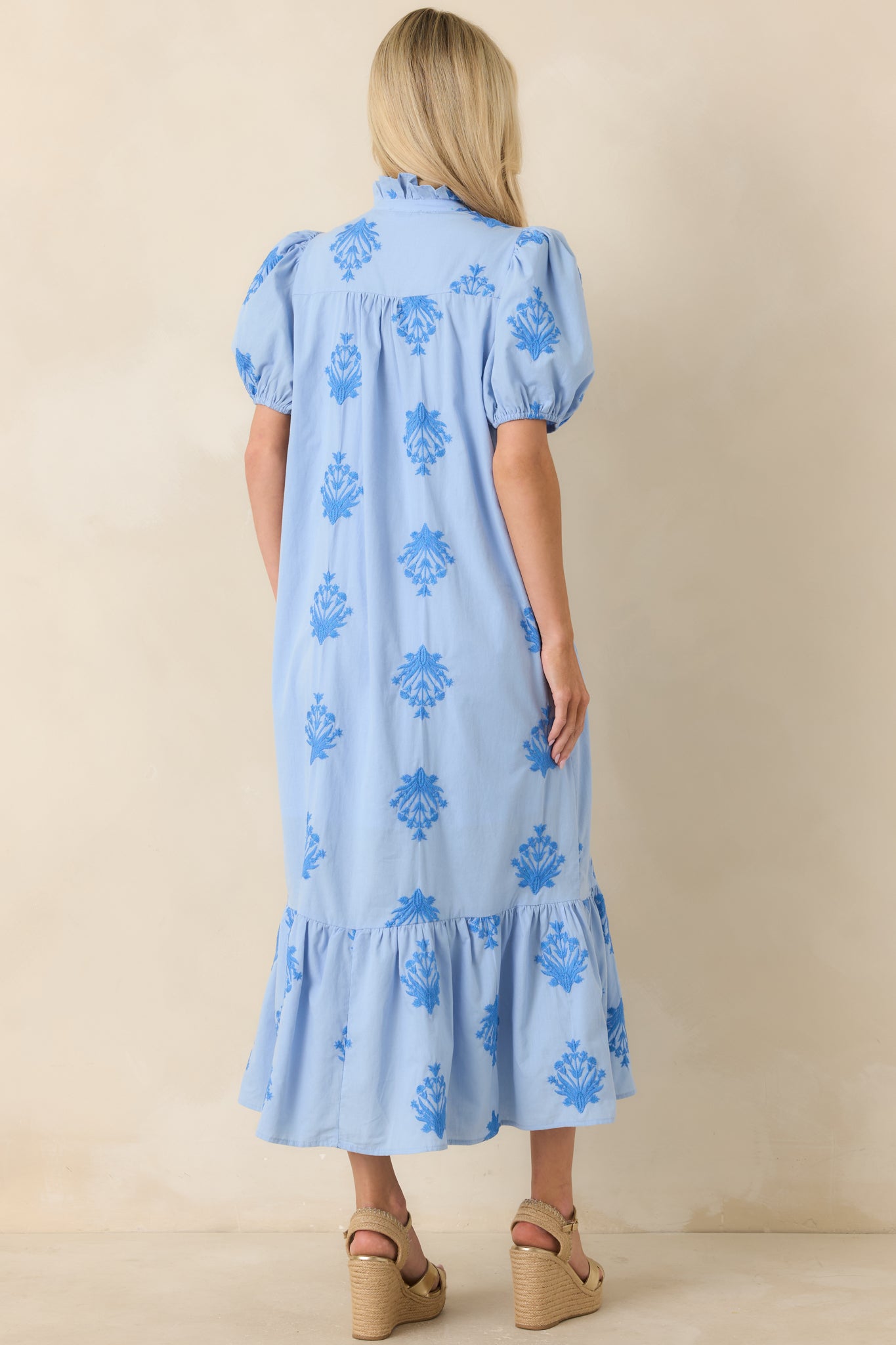 Sky blue cotton dress showing the back of the relaxed silhouette with puff sleeves, tonal embroidery, and a flowing ruffled hem.