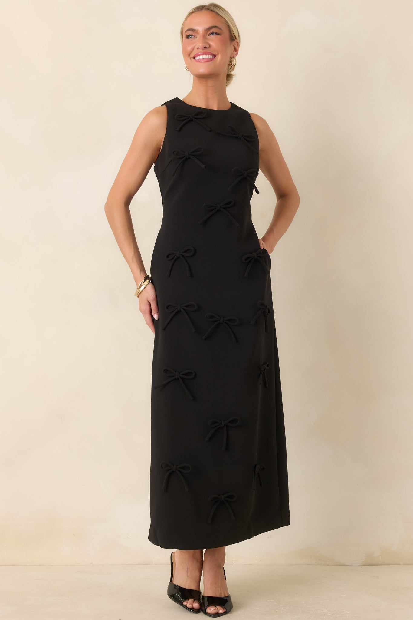 Sleeveless column maxi dress featuring a fitted bodice, tonal bow embellishments, and a sleek floor-length silhouette.