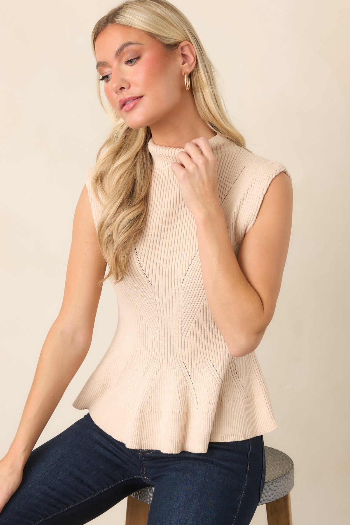 Sleeveless ecru knit top with a fitted waist and softly flared peplum hem.