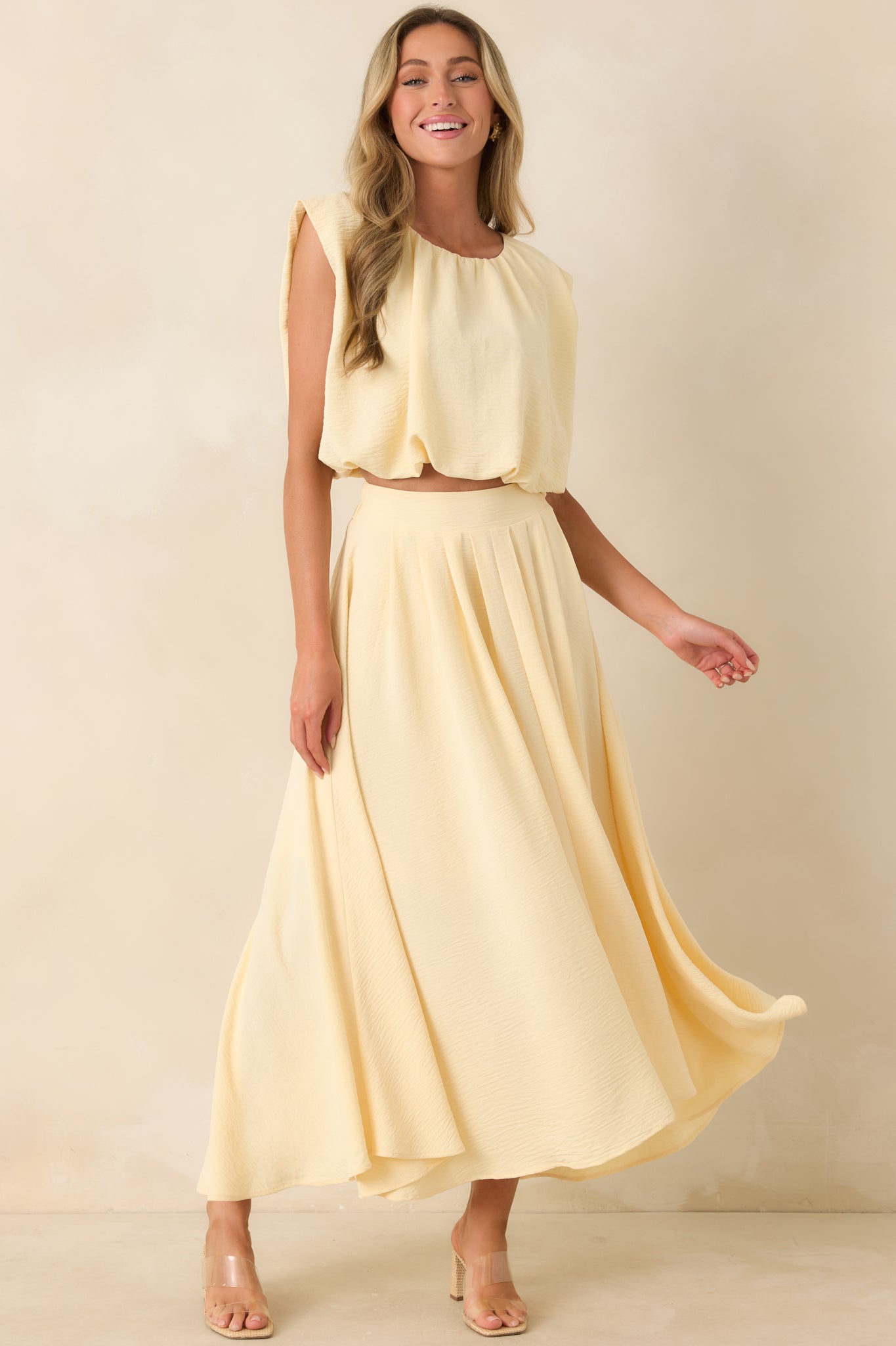 Sleeveless pale yellow cropped top with a relaxed draped fit, gathered neckline detail, and stretchy hemline.