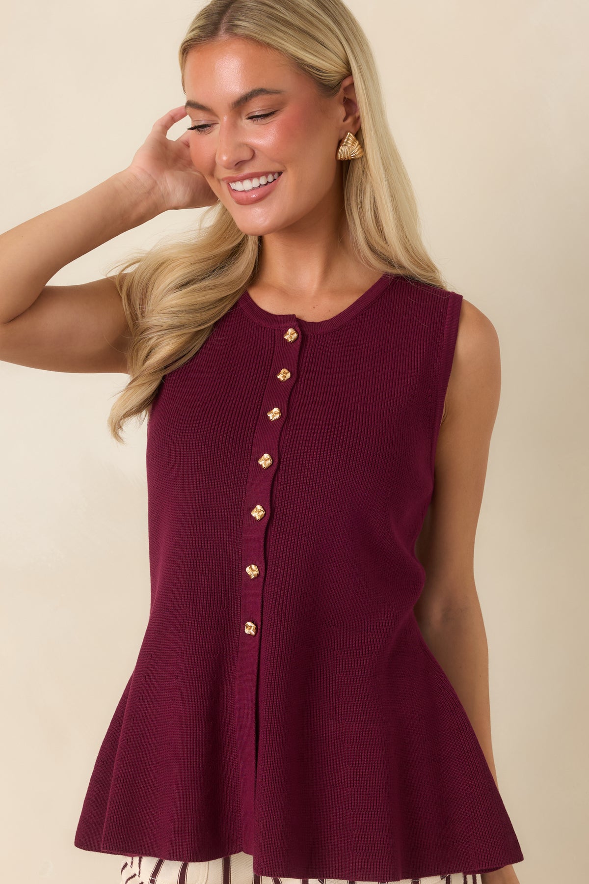 Partial view of the sleeveless top featuring decorative button details and a feminine peplum shape.