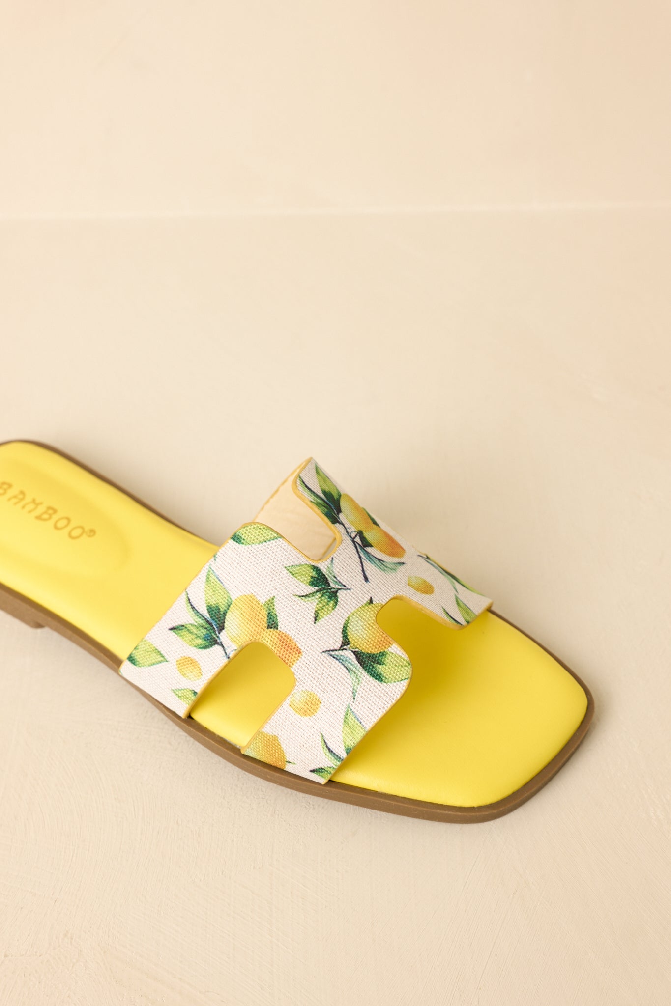 Close-up of slide sandals showcasing detailed fruit print on the wide strap, smooth faux leather base, and flat sole