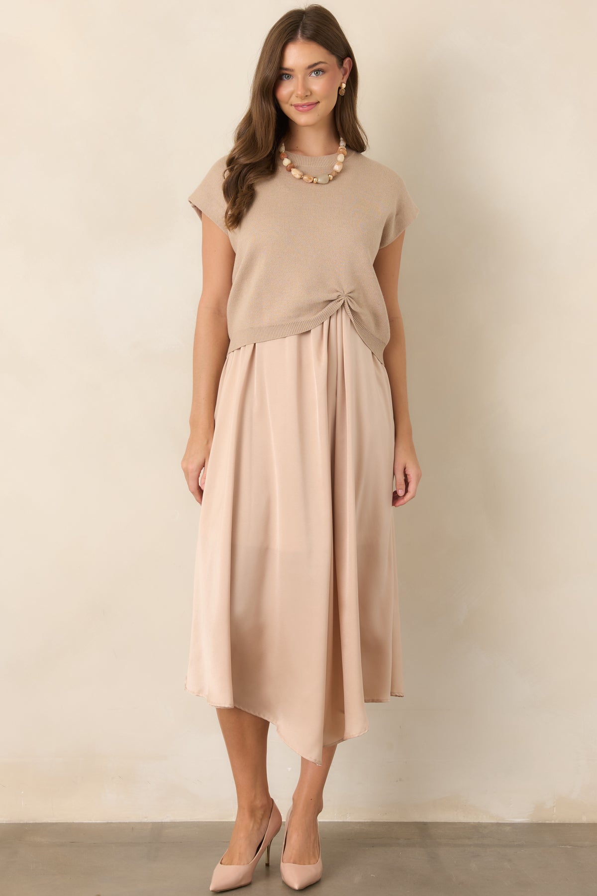 Soft beige knit top showcasing a polished crew neckline, cap-style sleeves, easy fit, and distinctive cinched detail at the front hem.