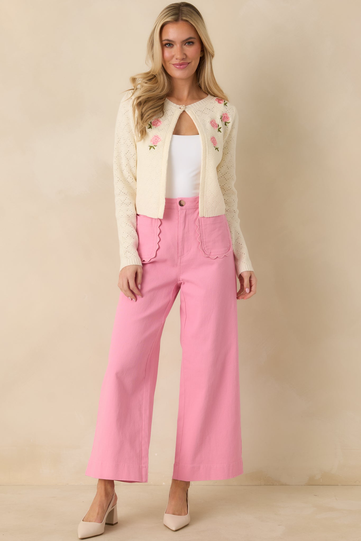Soft ivory knit cardigan embroidered with pink rose blooms throughout, finished with a pearl-style button closure at the neckline for a vintage-inspired touch.