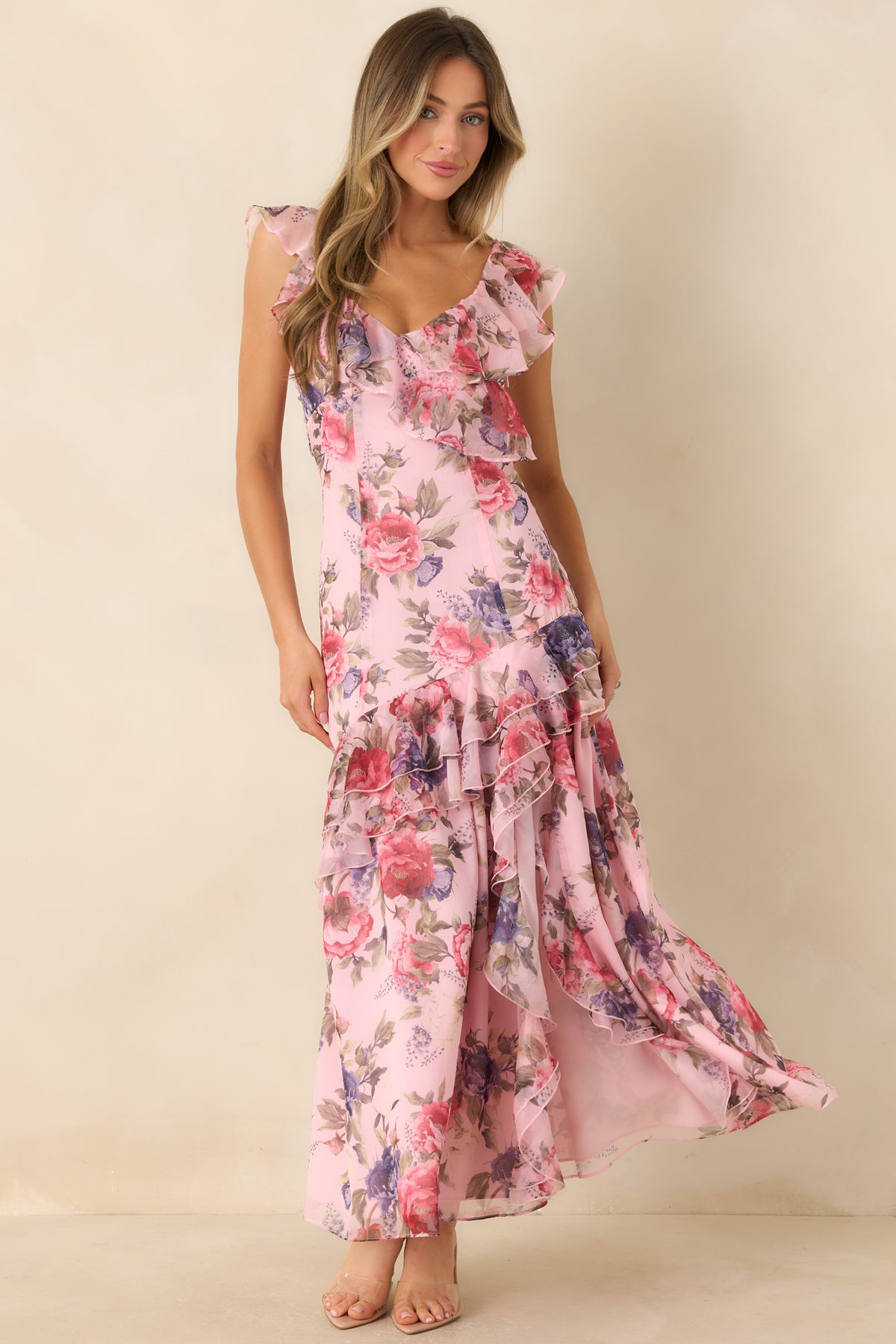 Soft pink floral maxi dress with rose pink and purple blooms, green foliage, and fluttering ruffles along the V-neckline.