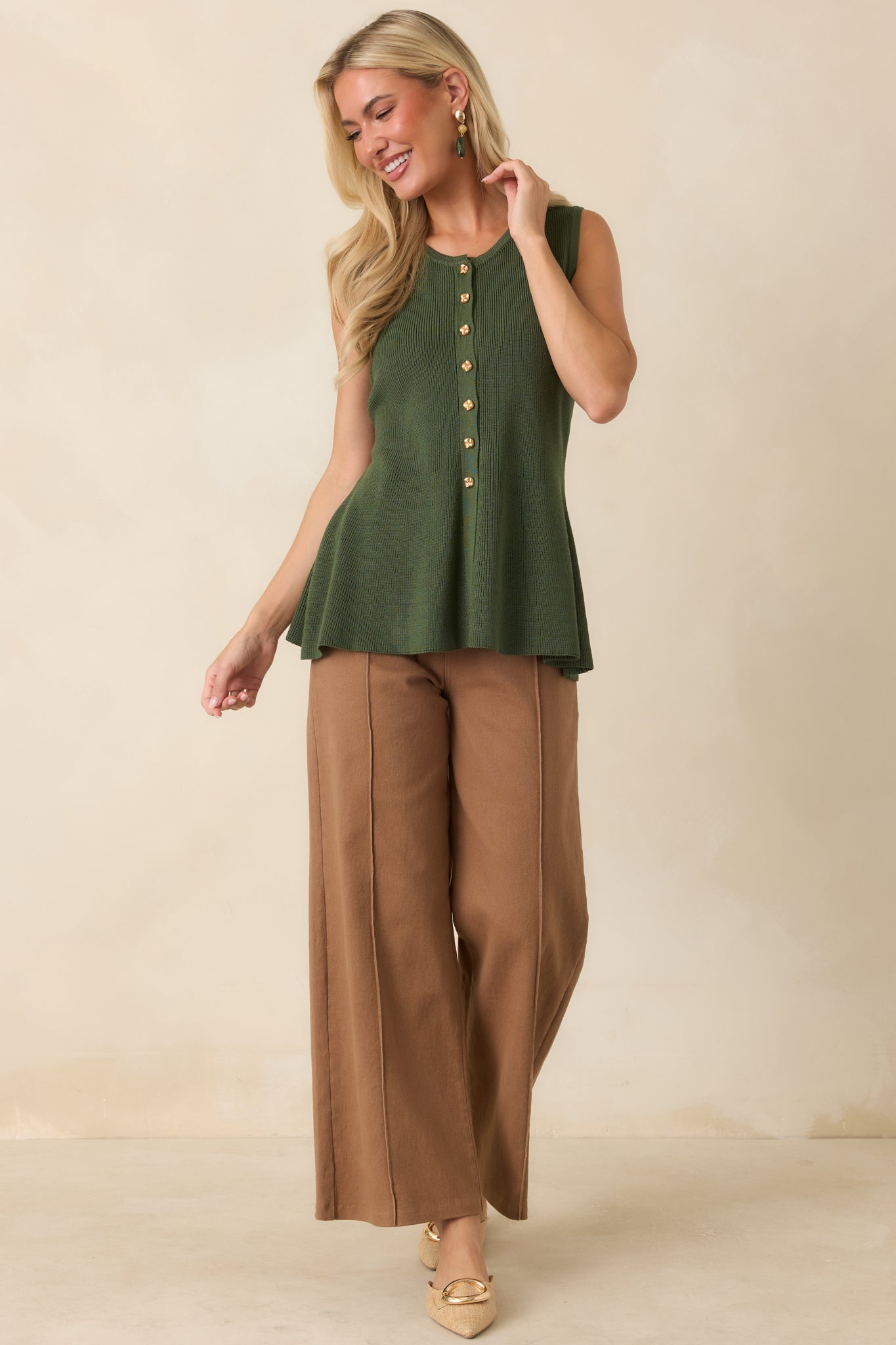 Soft stretch knit top featuring a sleeveless silhouette, fitted bodice, gold-tone buttons, and a feminine peplum hem.