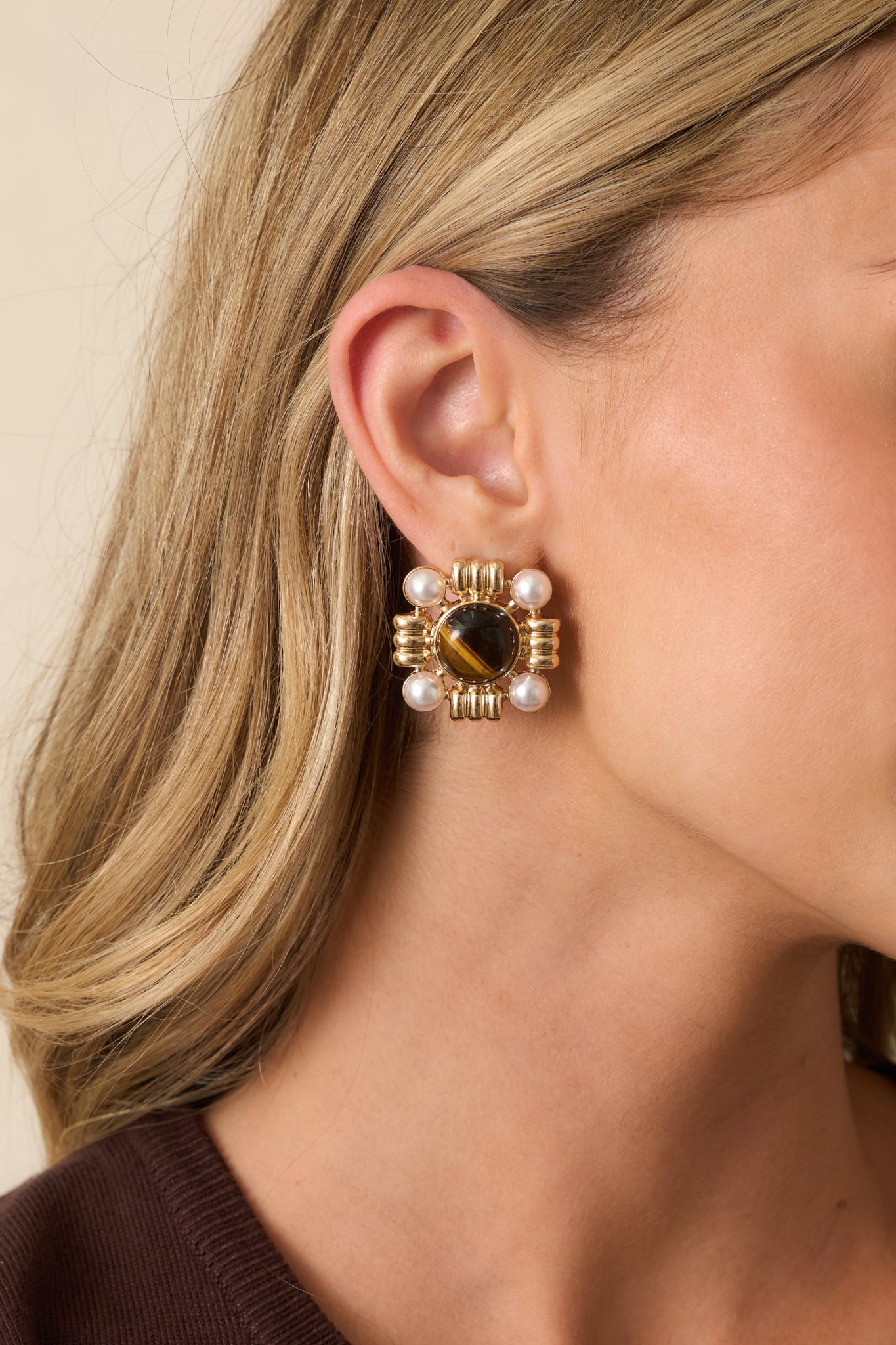 A cropped front view showing the square earrings with a brown marbled center stone, ivory faux pearls at each corner, and textured gold accents in between.