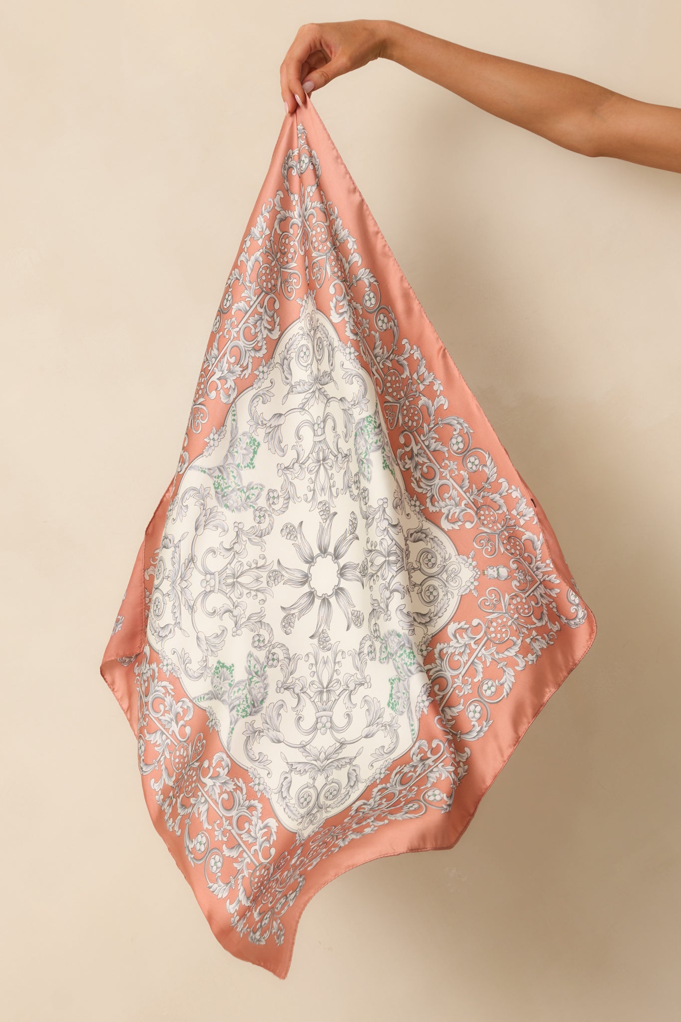 A full view of the square scarf with a rose pink border, ornate grey scrollwork and floral motif, subtle green accents, and smooth satin finish.