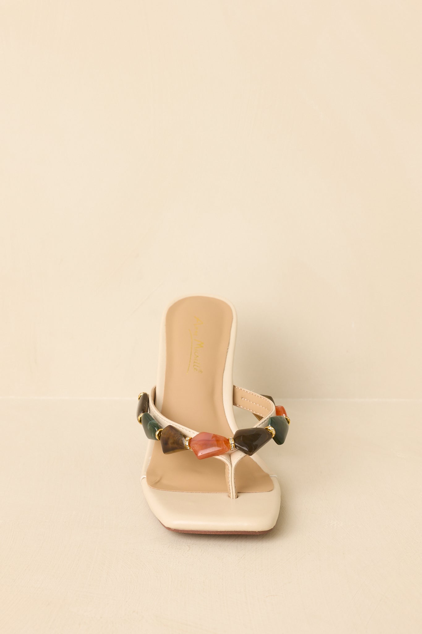 Square toe heeled sandals displayed on a beige background, showcasing embellished strap and structured heel