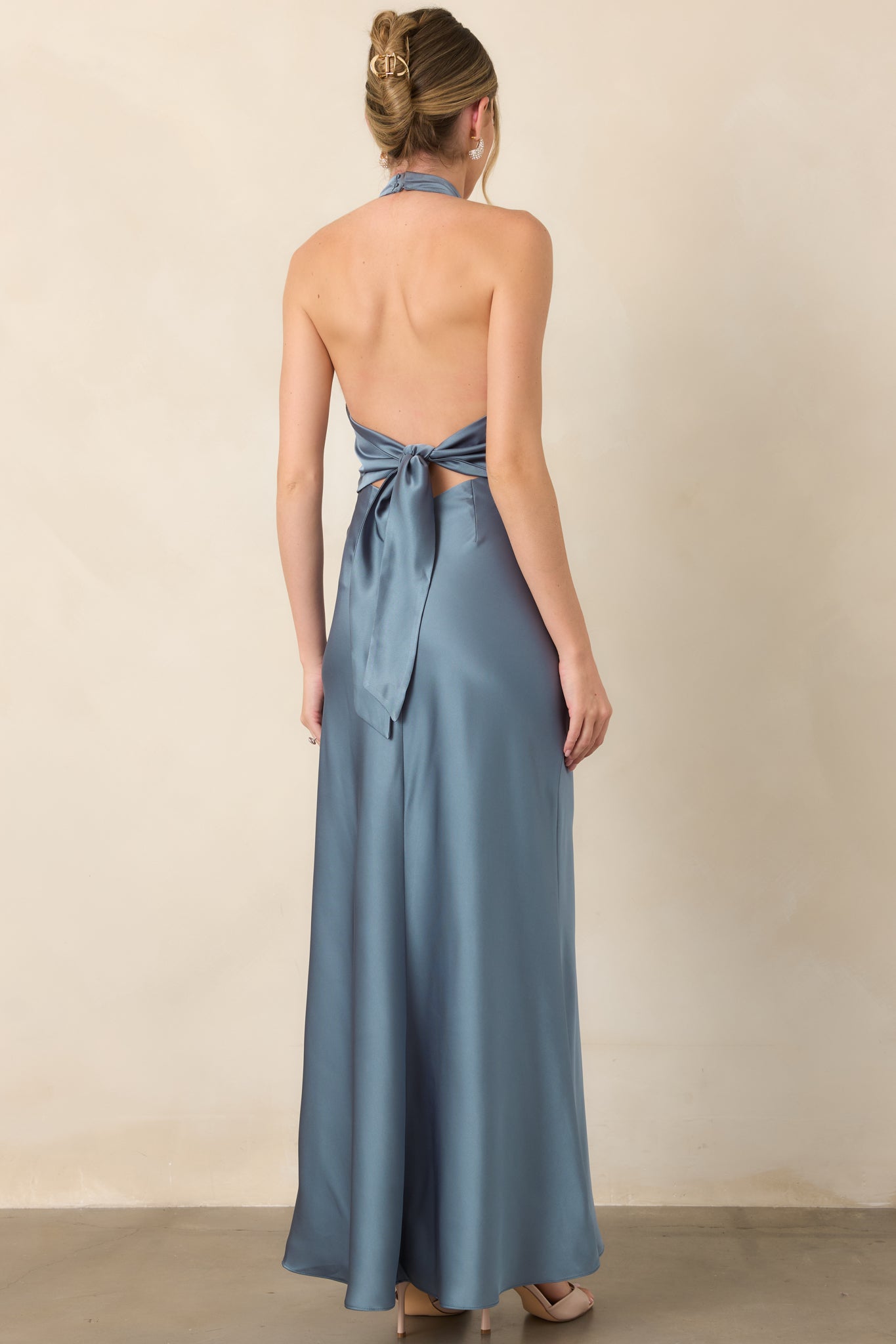 Rear view of the steel blue satin maxi dress showcasing its open back and dramatic self-tie detail above the flowing skirt.