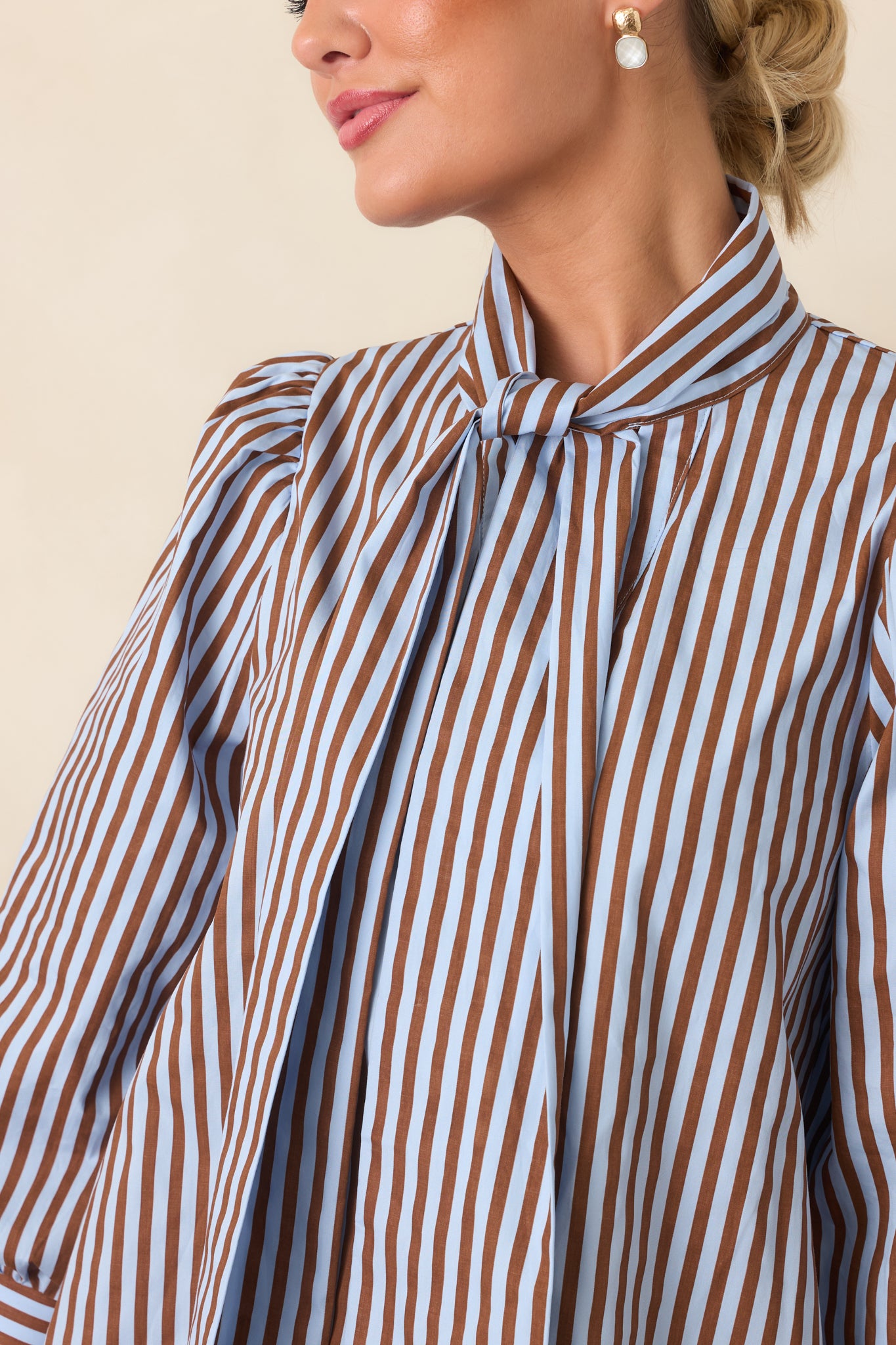 Close-up of the striped blouse showing the self-tie neckline, button-front closure, and gathered shoulder detail.