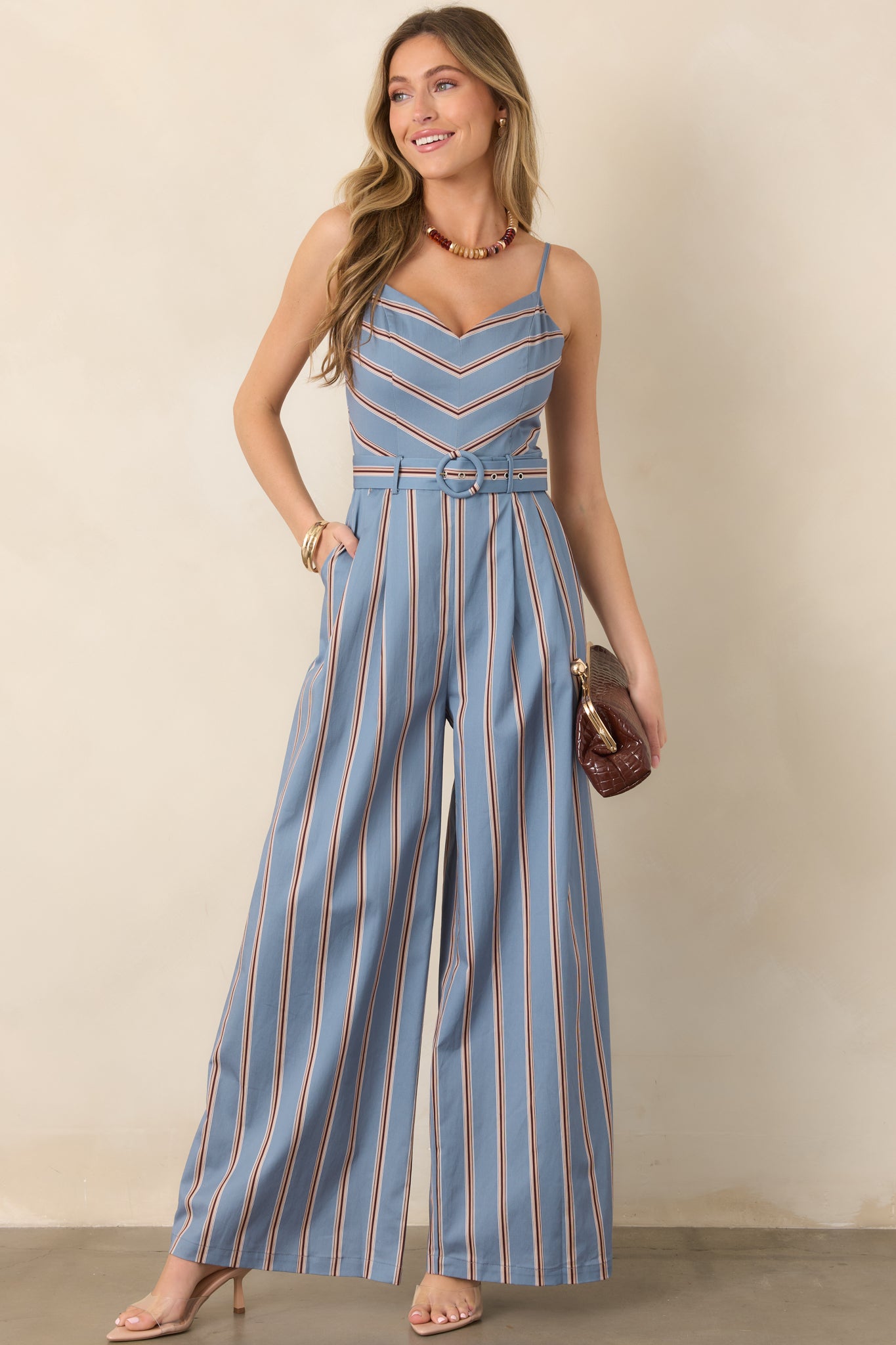 Striped jumpsuit featuring a sweetheart neckline, fitted chevron-patterned bodice, straight vertical leg stripes, and a covered round buckle belt.