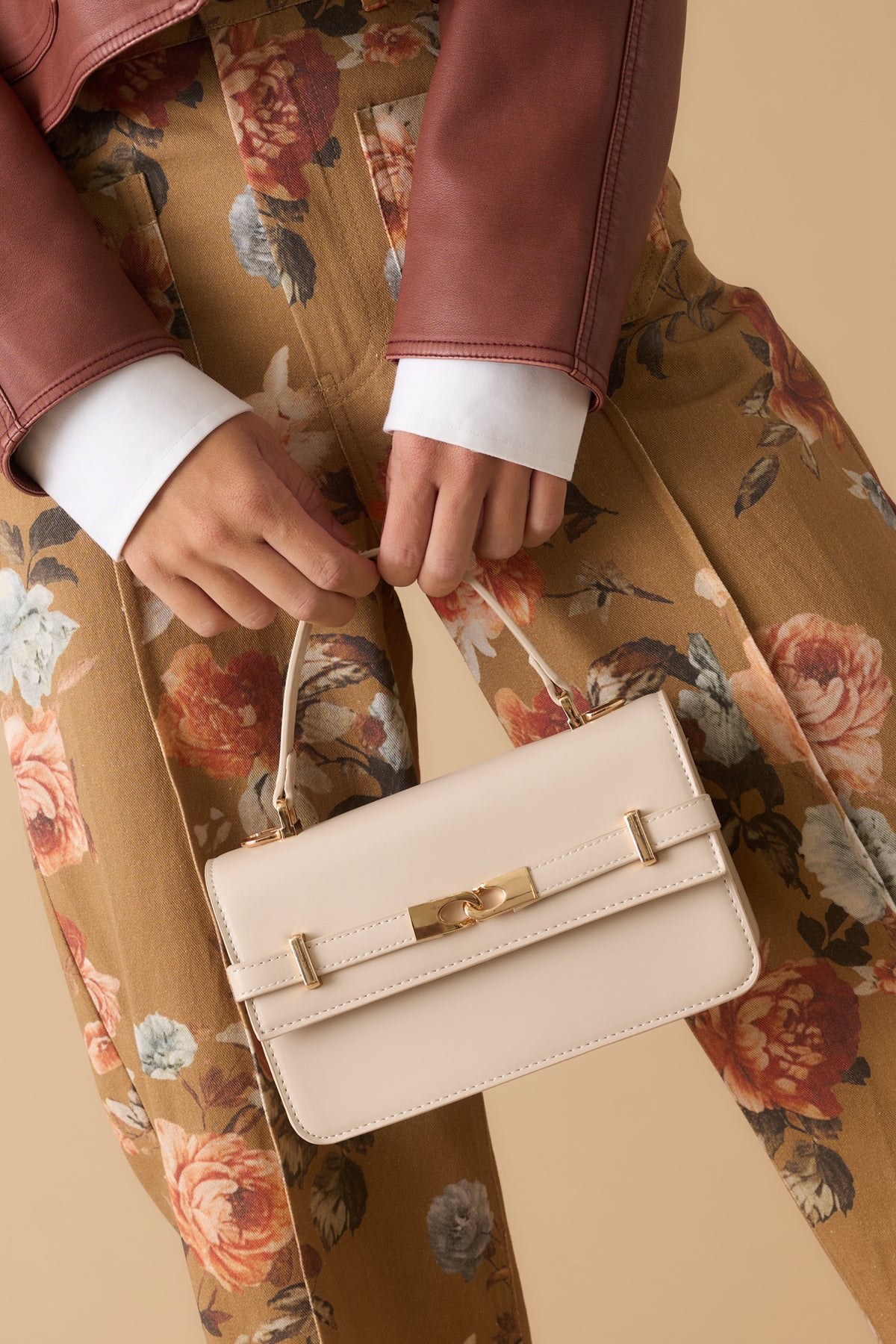 Structured faux leather handbag featuring polished gold-tone hardware, a top handle, and elegant front belt detail.