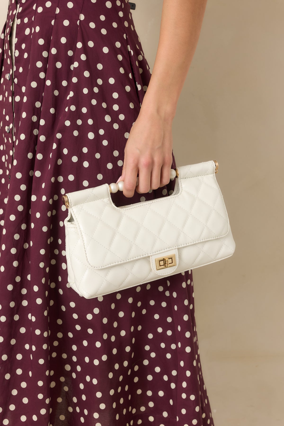 Faux leather handbag showcasing the pearl top handle and polished structured silhouette.