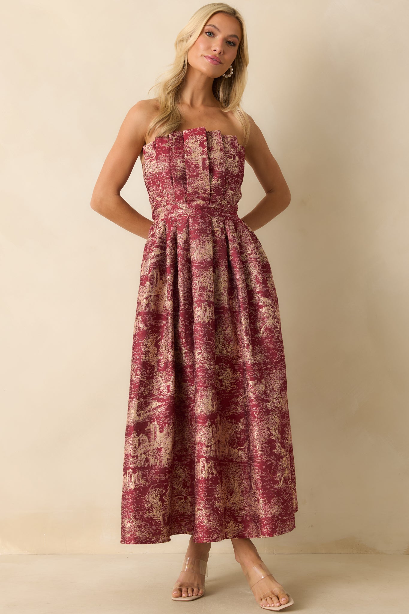 Structured strapless burgundy dress featuring a fitted pleated bodice, flowing A-line skirt, and intricate ivory jacquard design.