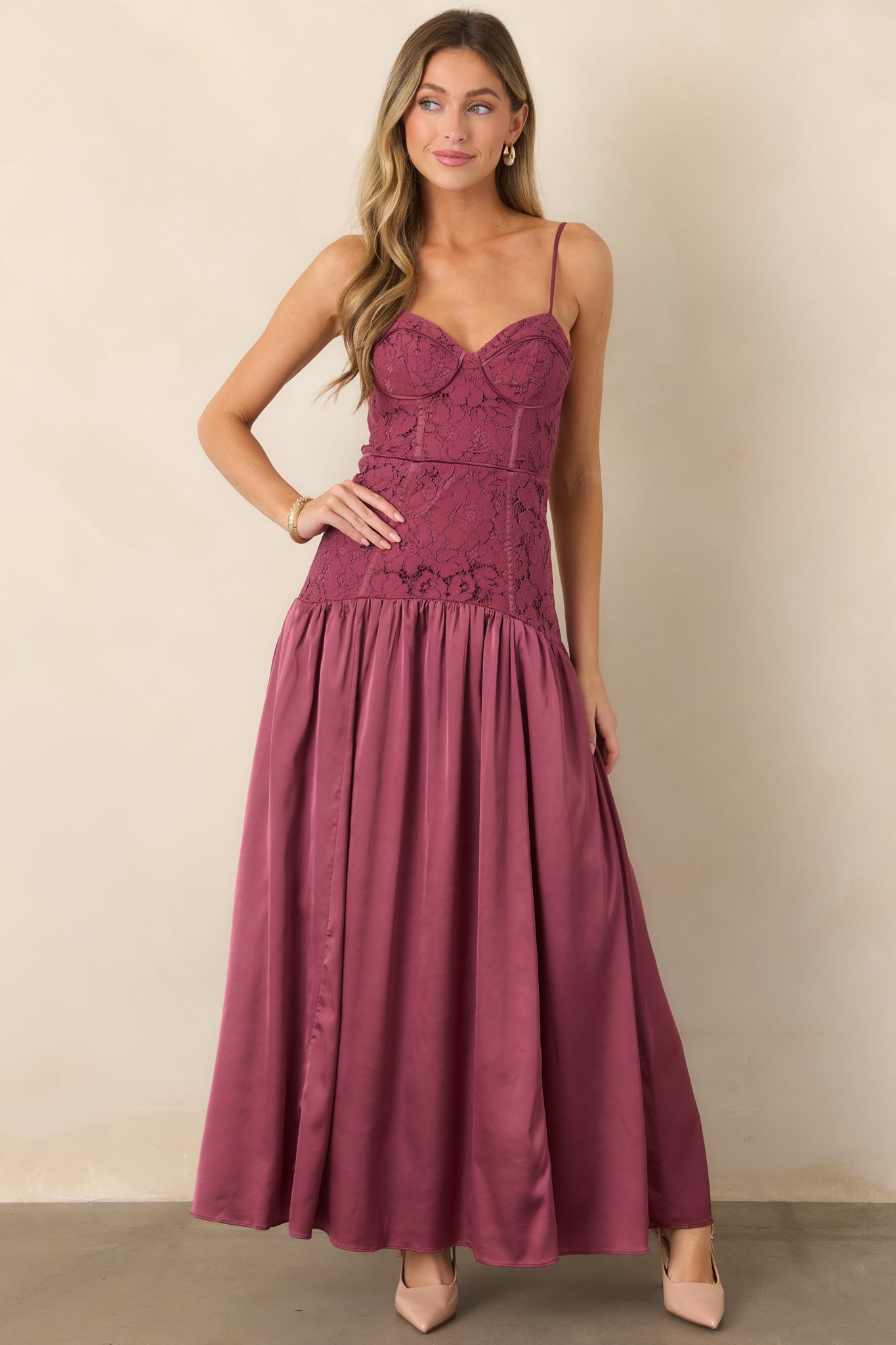 Floor-length satin dress with a defined sweetheart bustier, slim straps, elongated dropped waist, and voluminous gathered skirt for graceful movement.