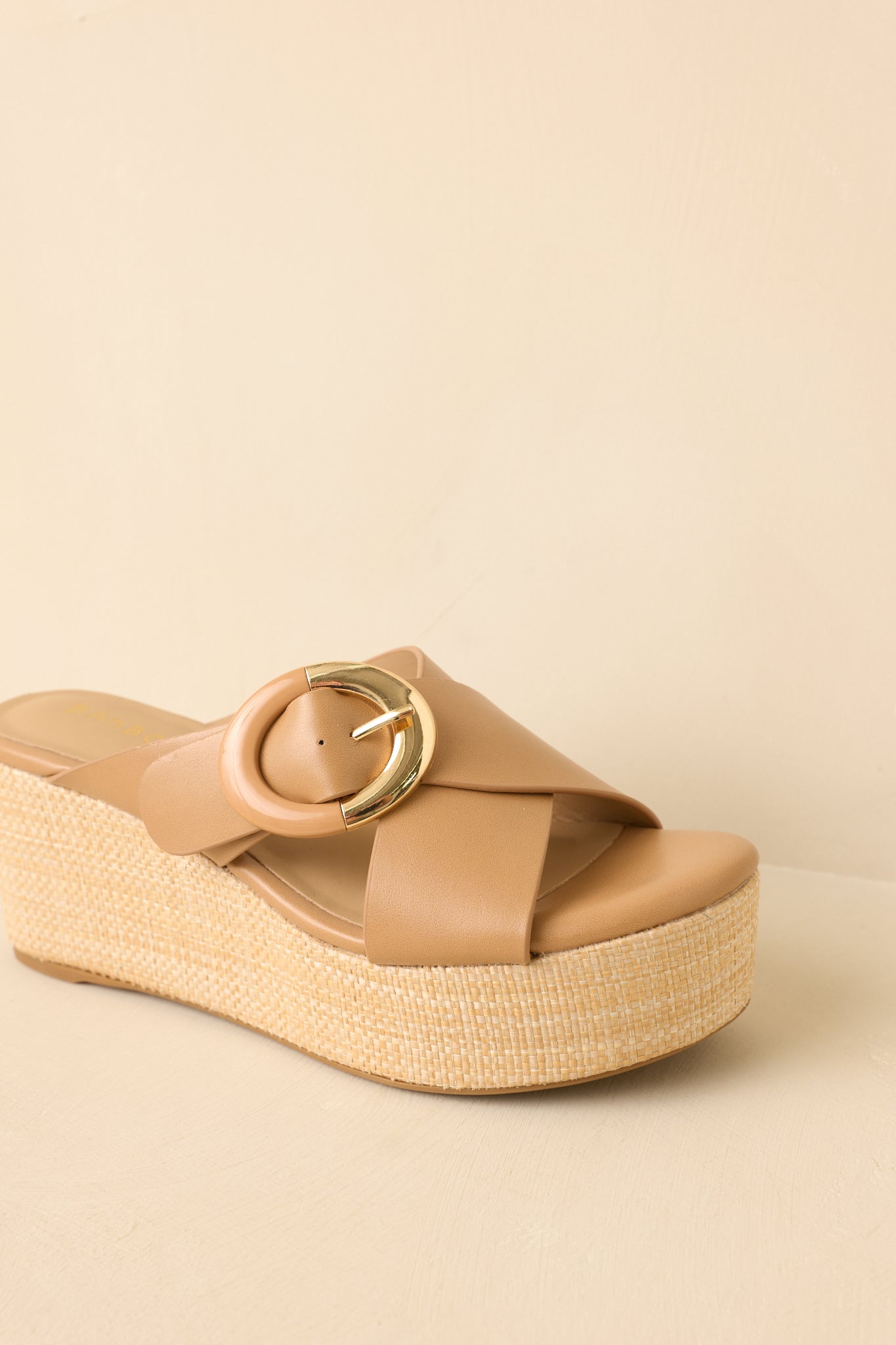 Front-facing view of tan faux leather wedges on a beige background highlighting the wide strap and buckle detail.