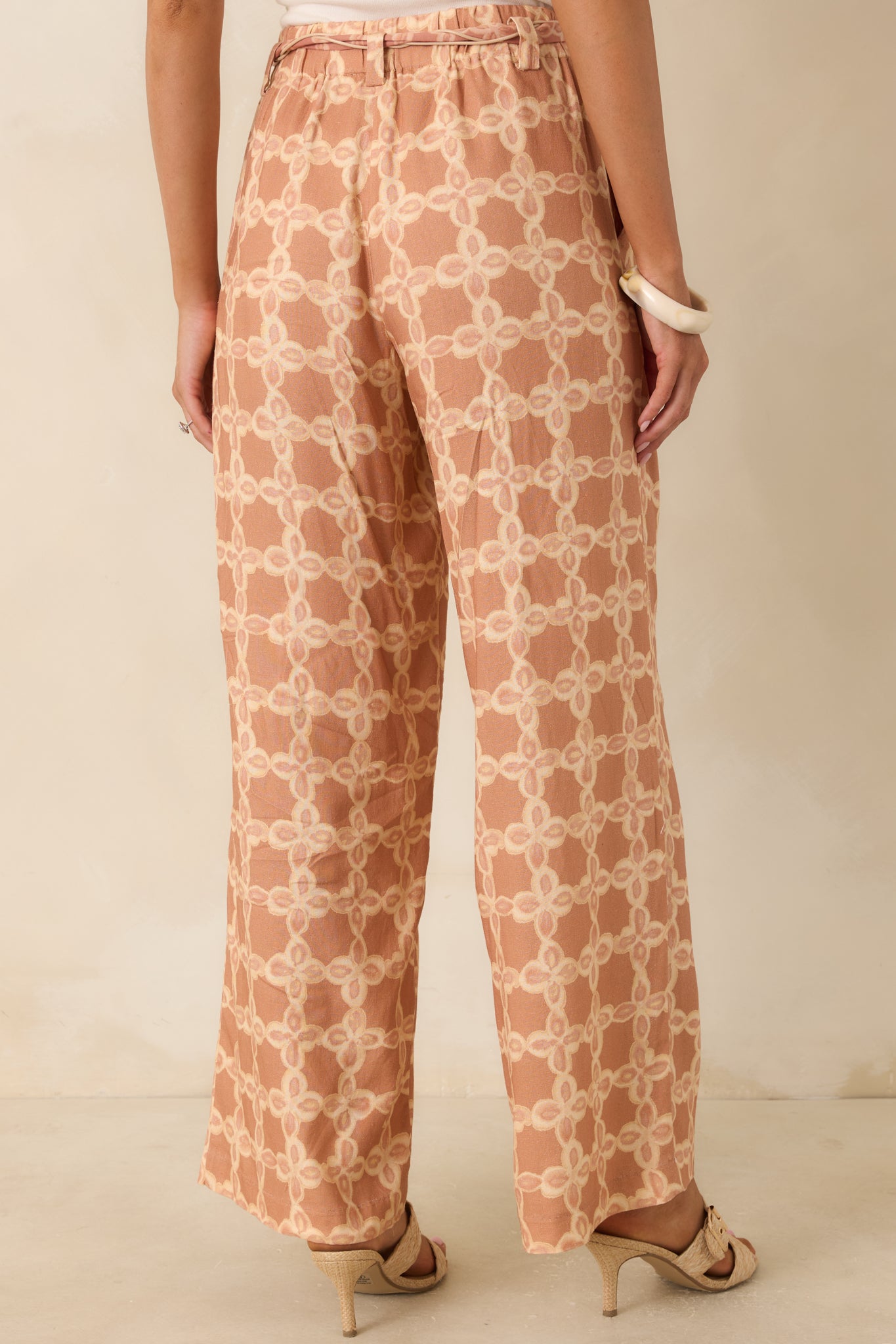 Back of the tan and ivory printed wide leg pants featuring back welt pockets and a tailored high-rise waistband.