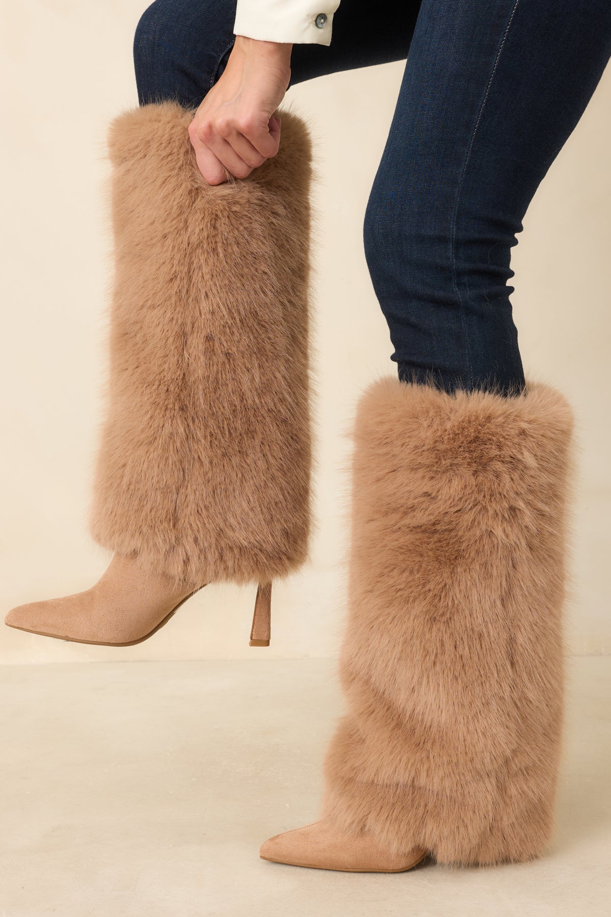 Tan knee-high boots with pointed toes, plush faux fur shafts, and slim stiletto heels.