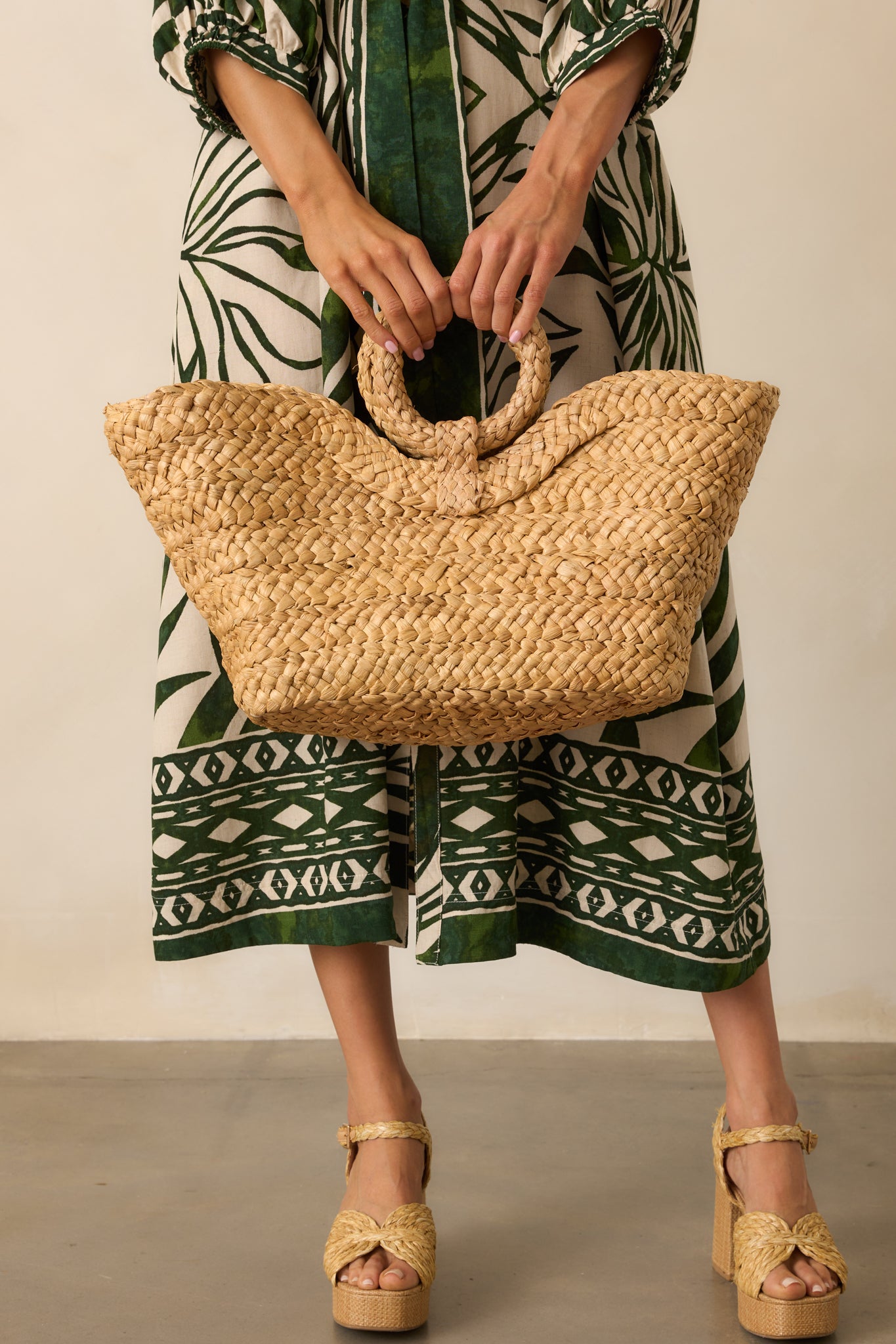 Full body front view showing the tan raffia handbag with an open tote design and circular woven handles.
