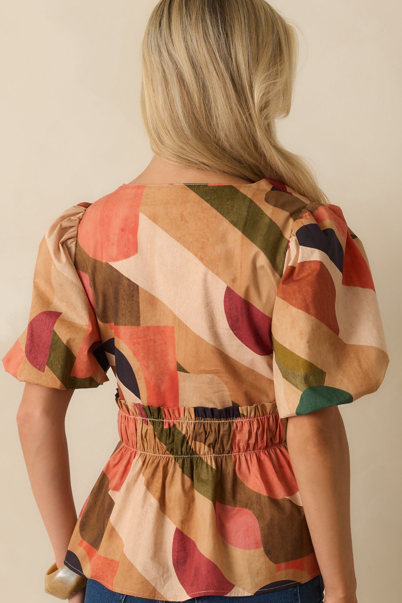 Rear view of the tan top showing peplum silhouette and elastic waist design.