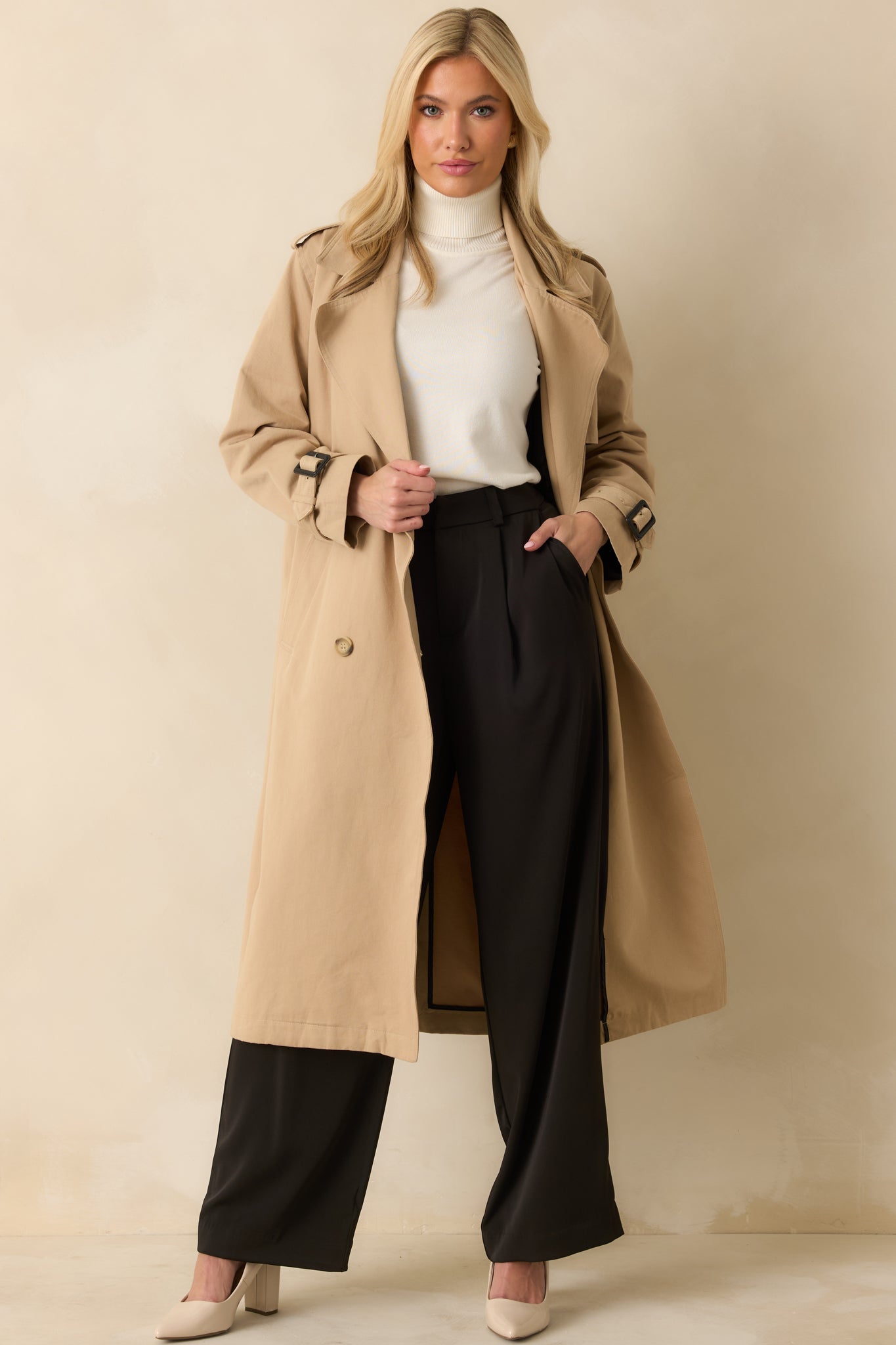 Front-facing view of the tan trench coat highlighting the double-breasted buttons, notched lapels, and tie belt.