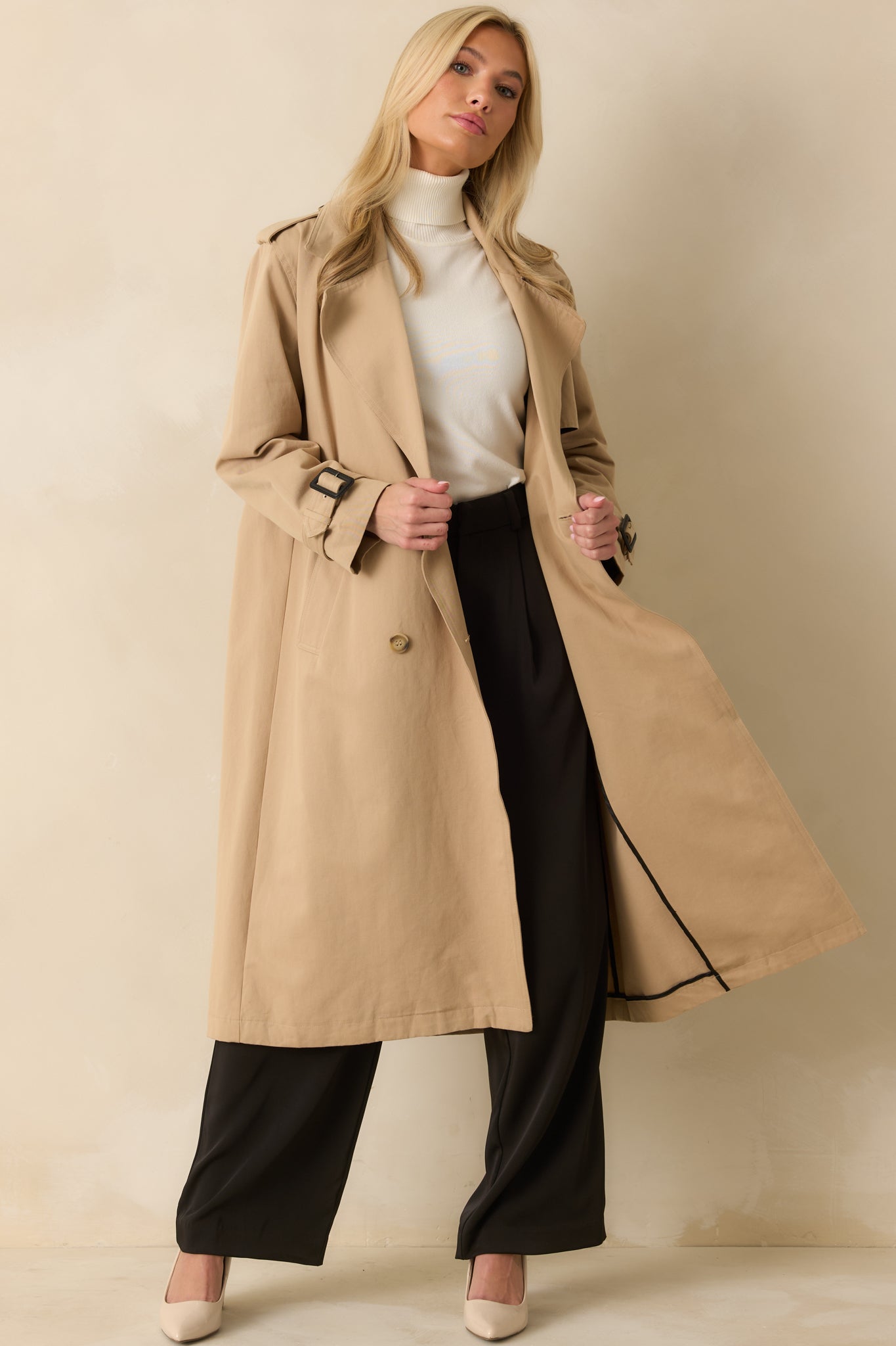 Tan trench coat displayed full length, showing side pockets, adjustable buckled cuffs, and classic storm flap.