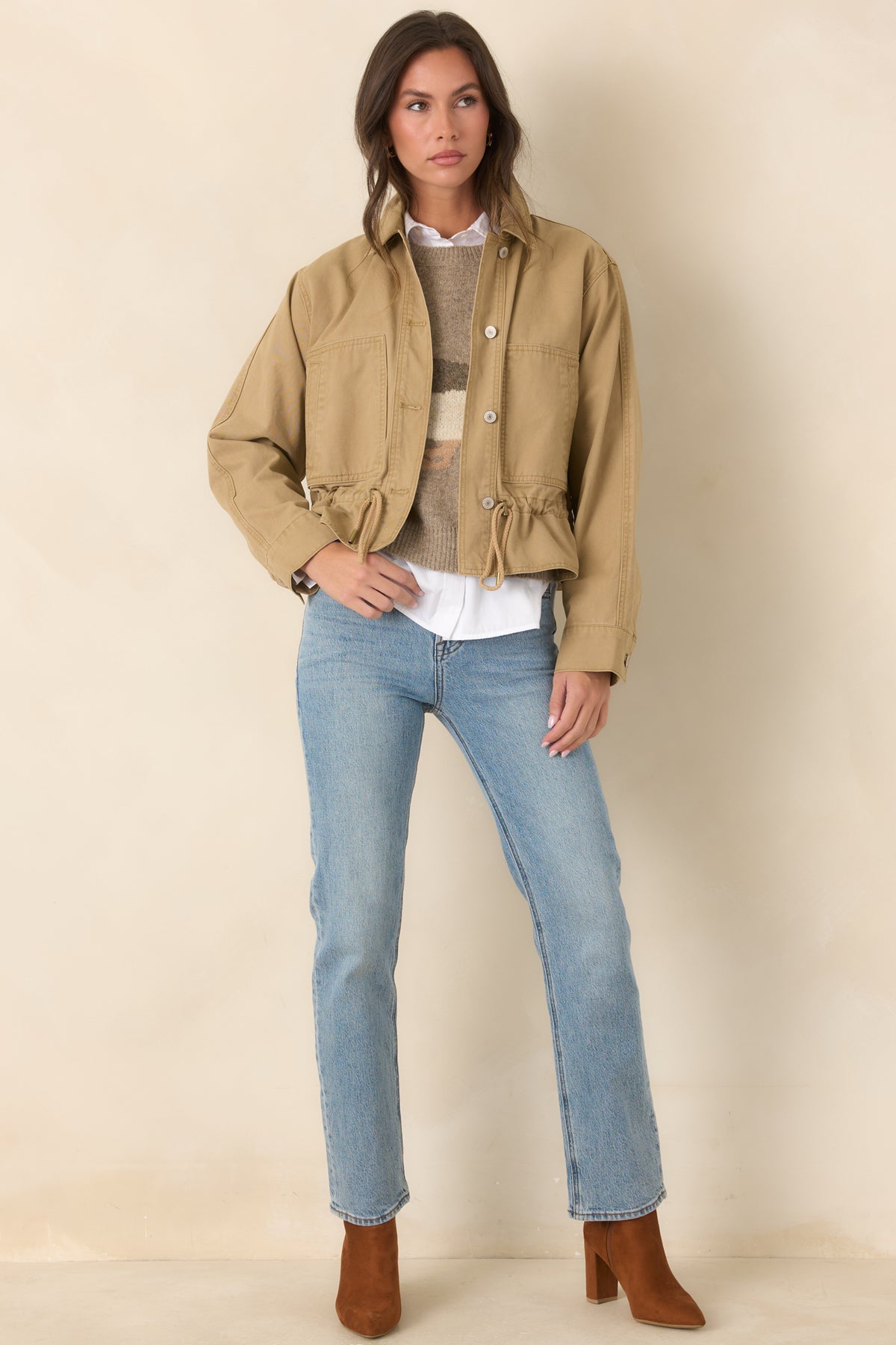 Tan utility jacket features a collared neckline, front button closures, large patch pockets, and an adjustable drawcord hem.