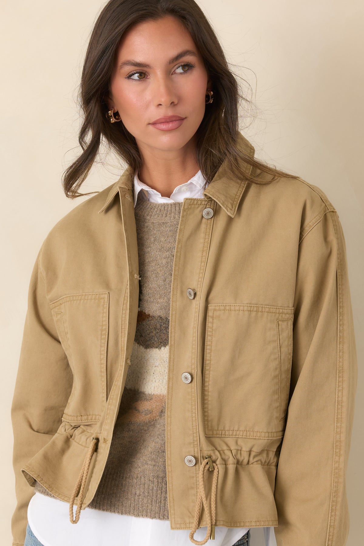 Large patch pockets add a functional detail to the front of this tan utility jacket.