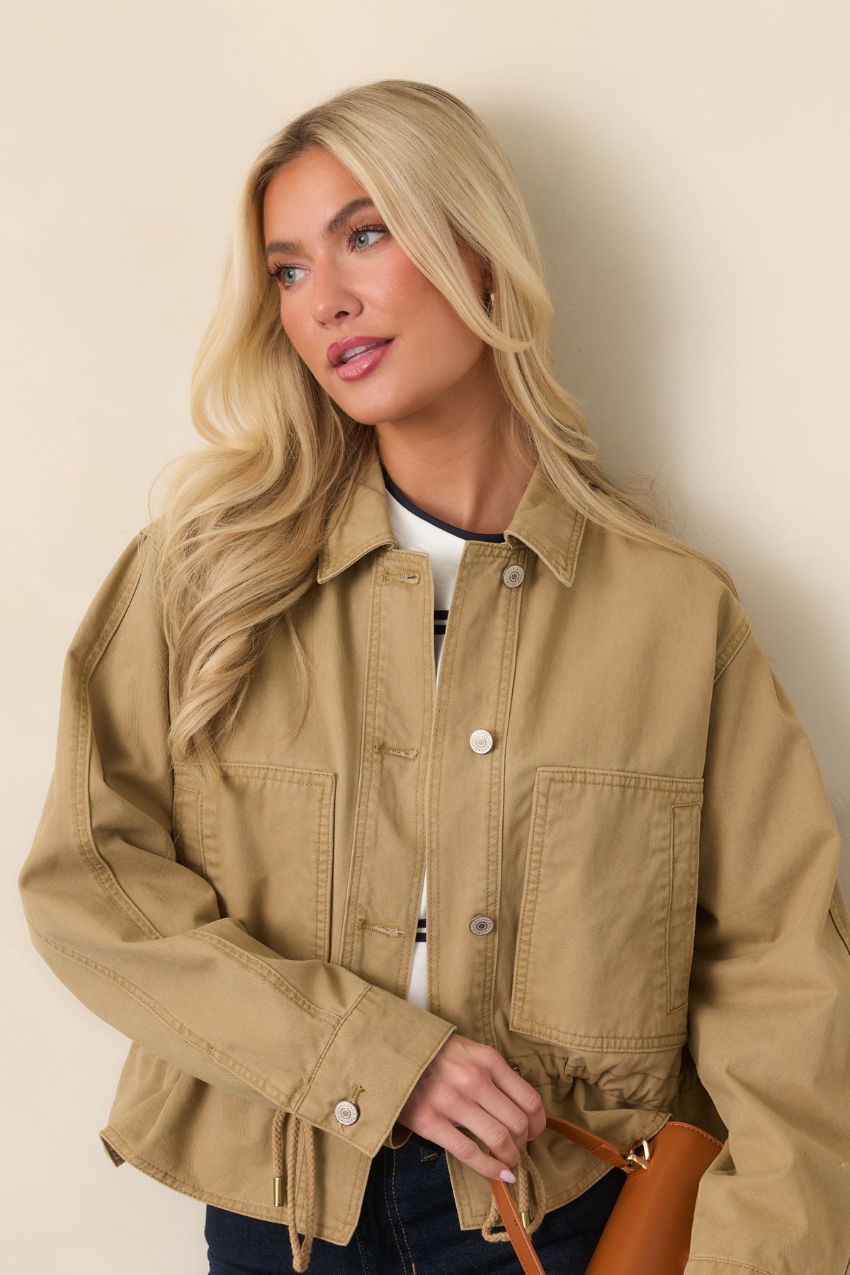 Close detail of the tan utility jacket showing a large patch pocket and button closure.