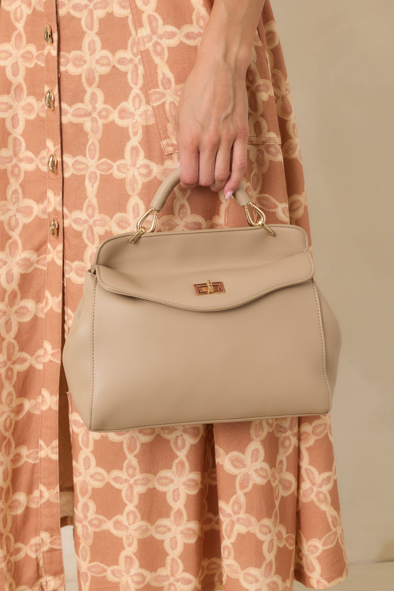 Taupe faux leather handbag featuring a structured silhouette, top handle, and gold-tone twist lock closure.