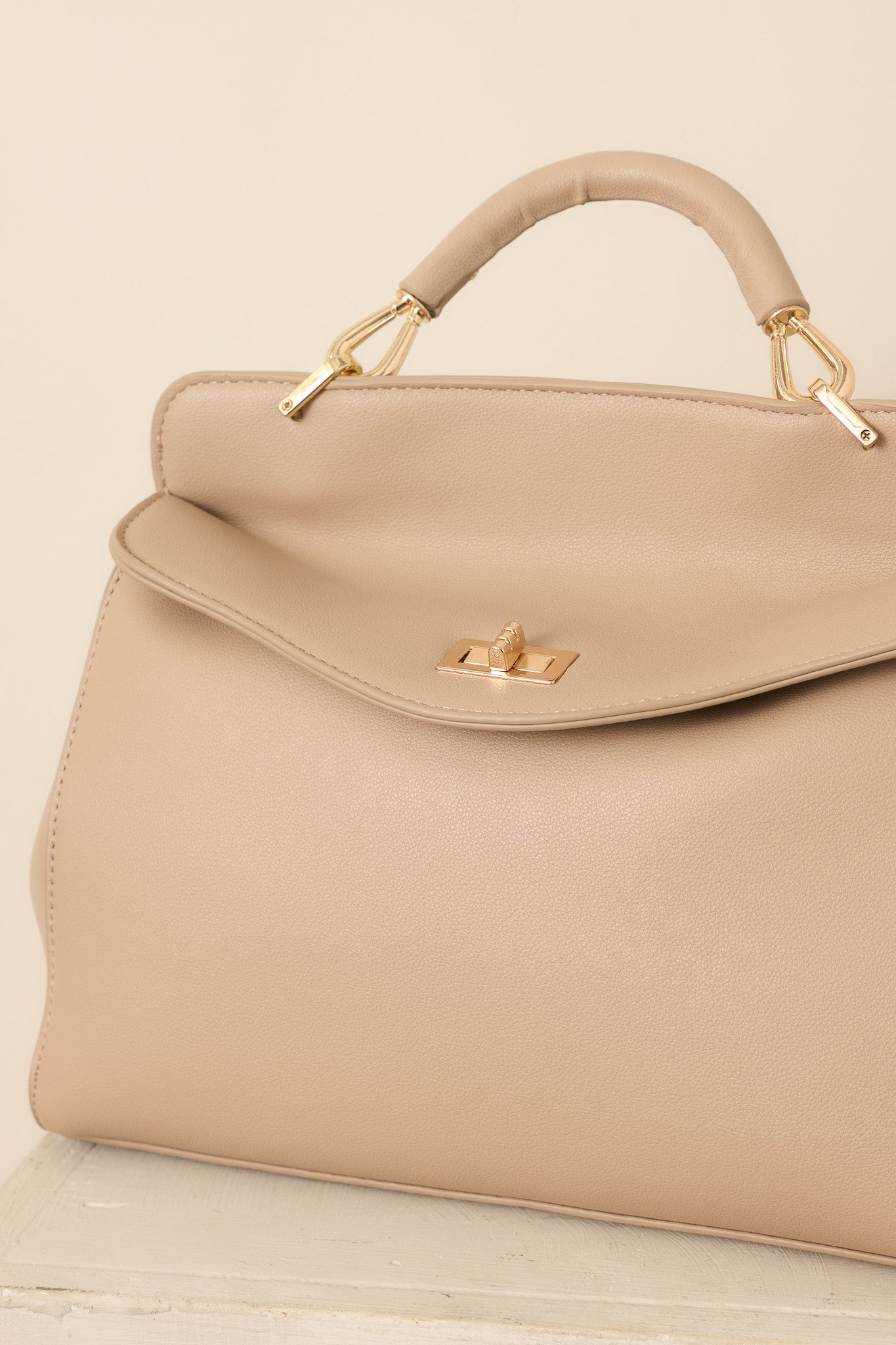 Close-up of the taupe handbag highlighting its gold-tone twist lock closure, textured faux leather finish, and structured construction.