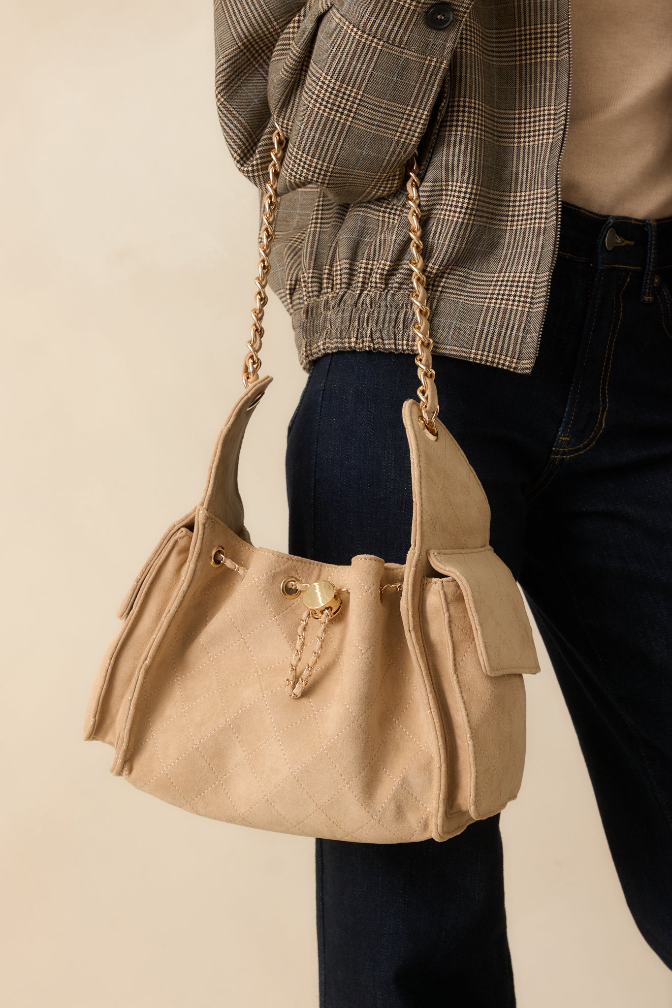 Taupe quilted faux leather purse with gold and faux leather cord drawstring, fold-over side pockets, and detachable strap.