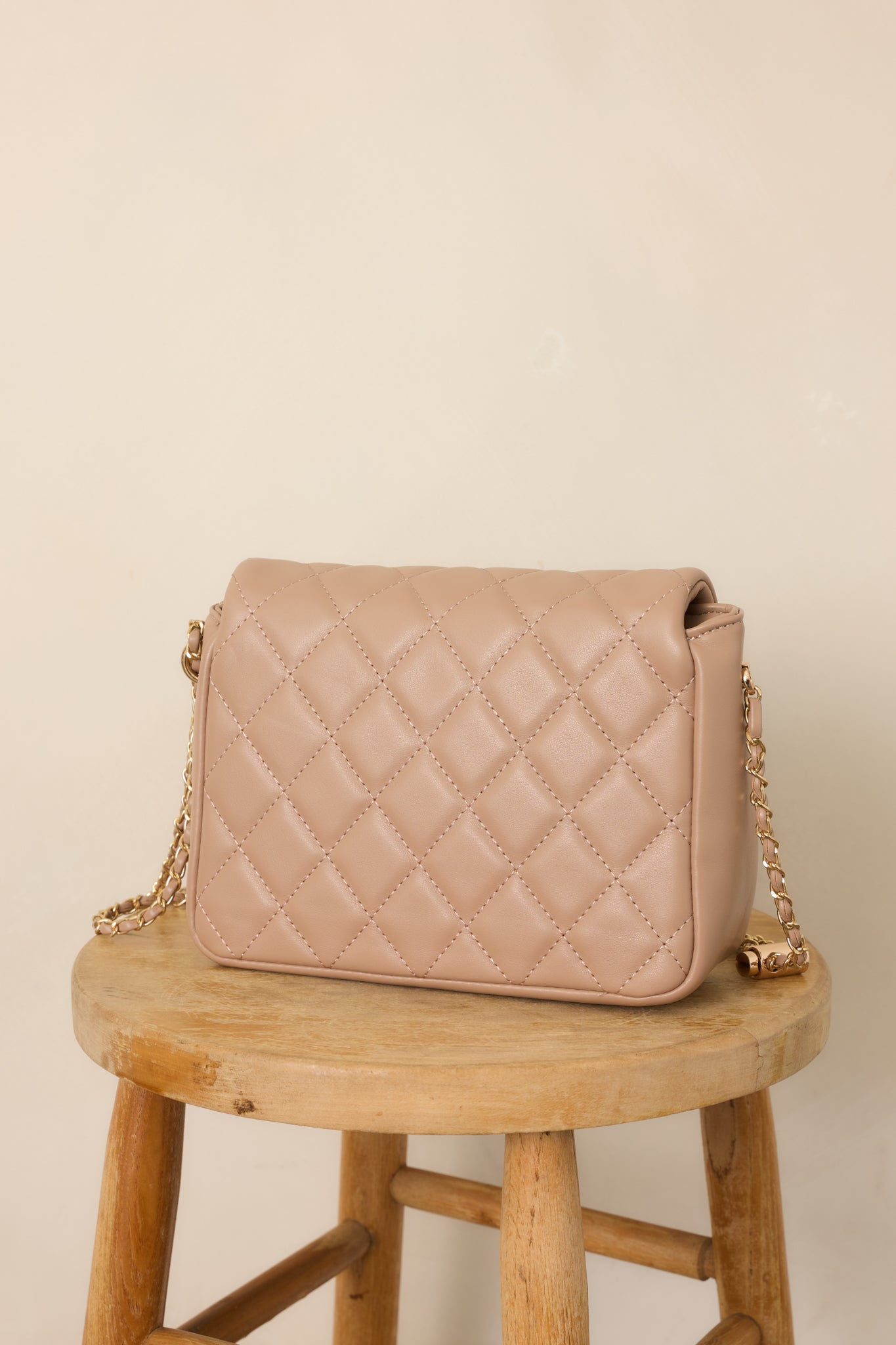 Rear view of the taupe handbag displaying its quilted exterior, compact structured shape, and clean finished back panel.
