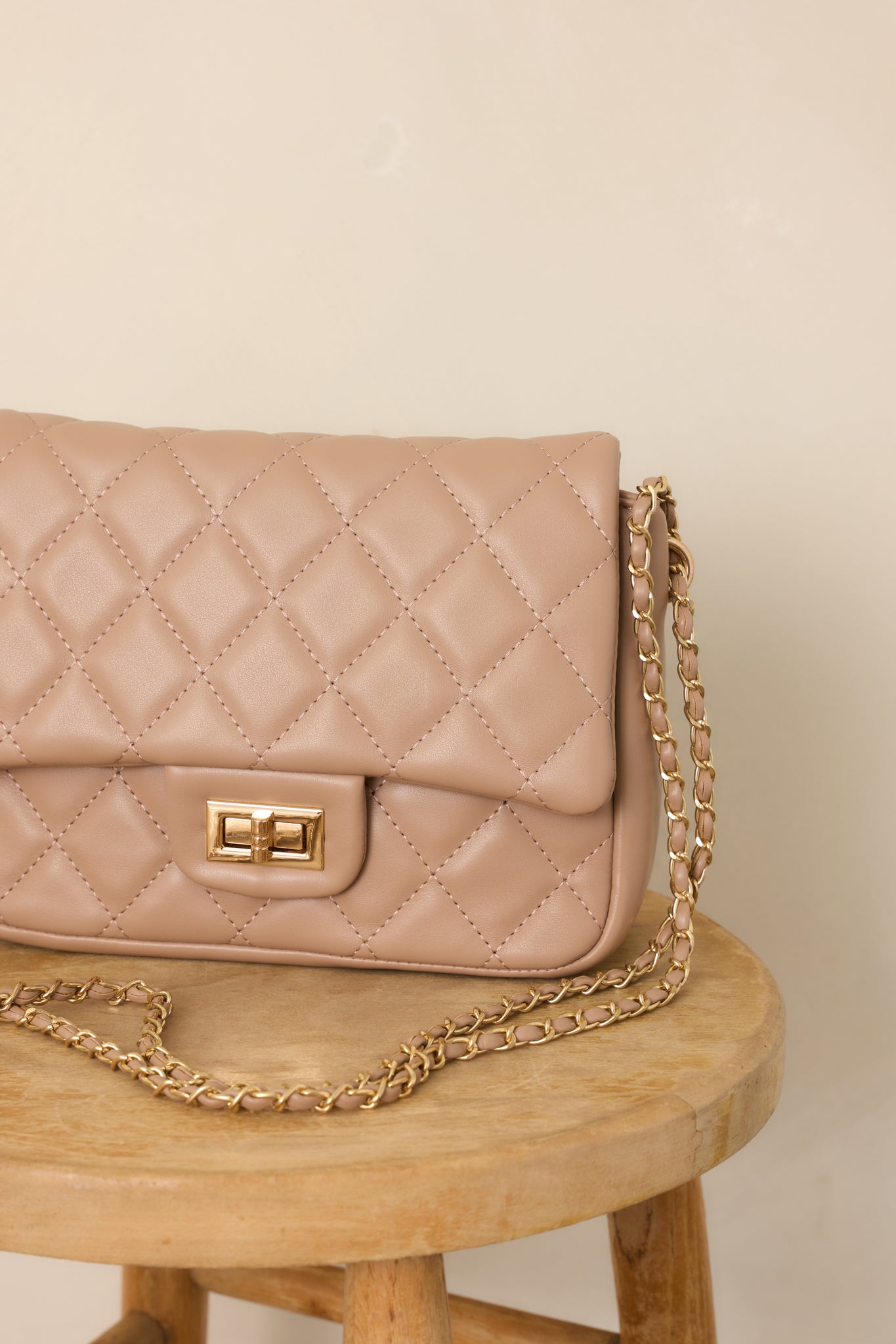Close-up of the taupe handbag’s quilted surface and front turn-lock closure, showcasing the contrasting textures and polished hardware.