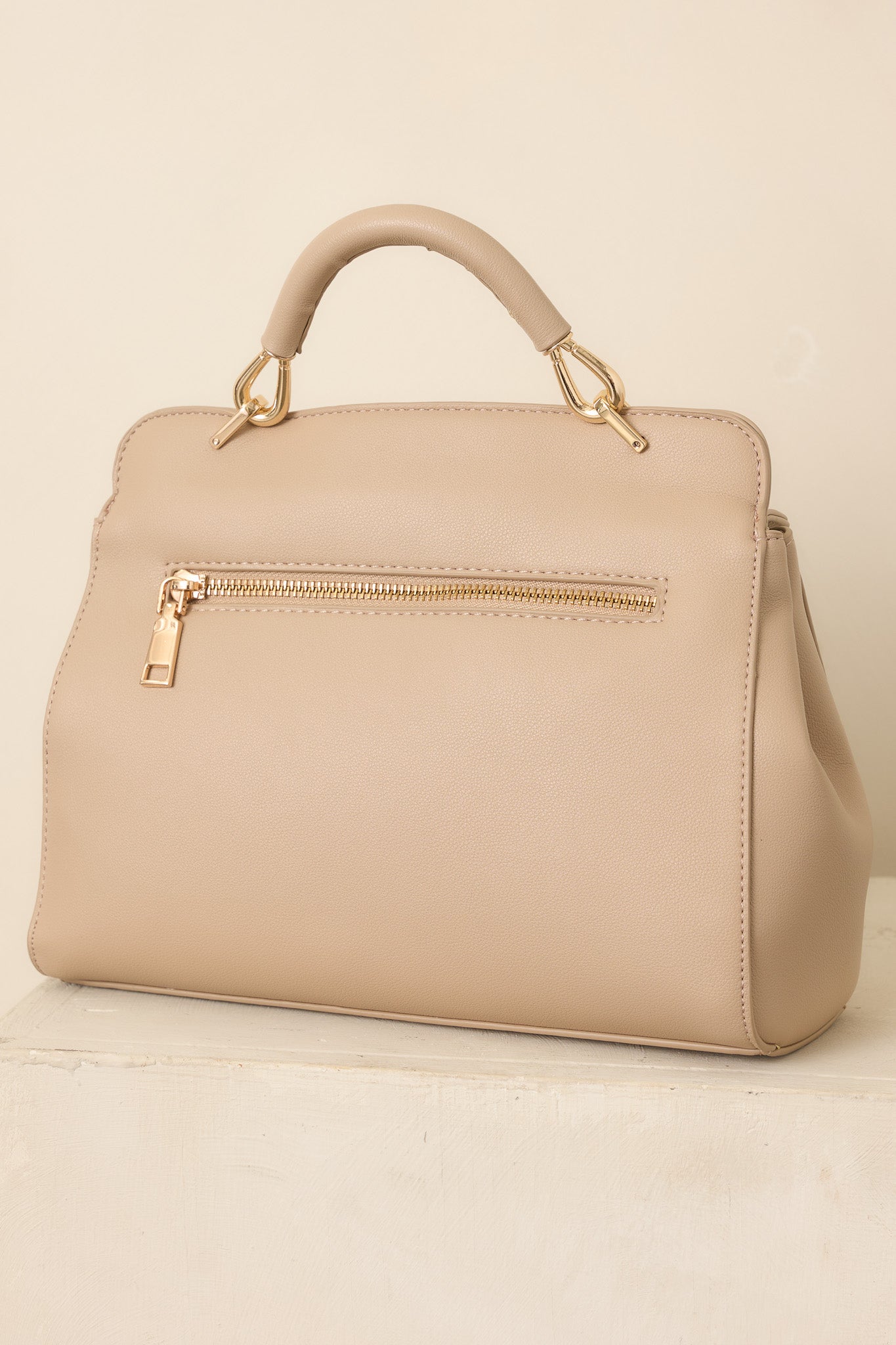 Rear view of the taupe faux leather handbag showcasing its structured silhouette, smooth back panel, and top handle.