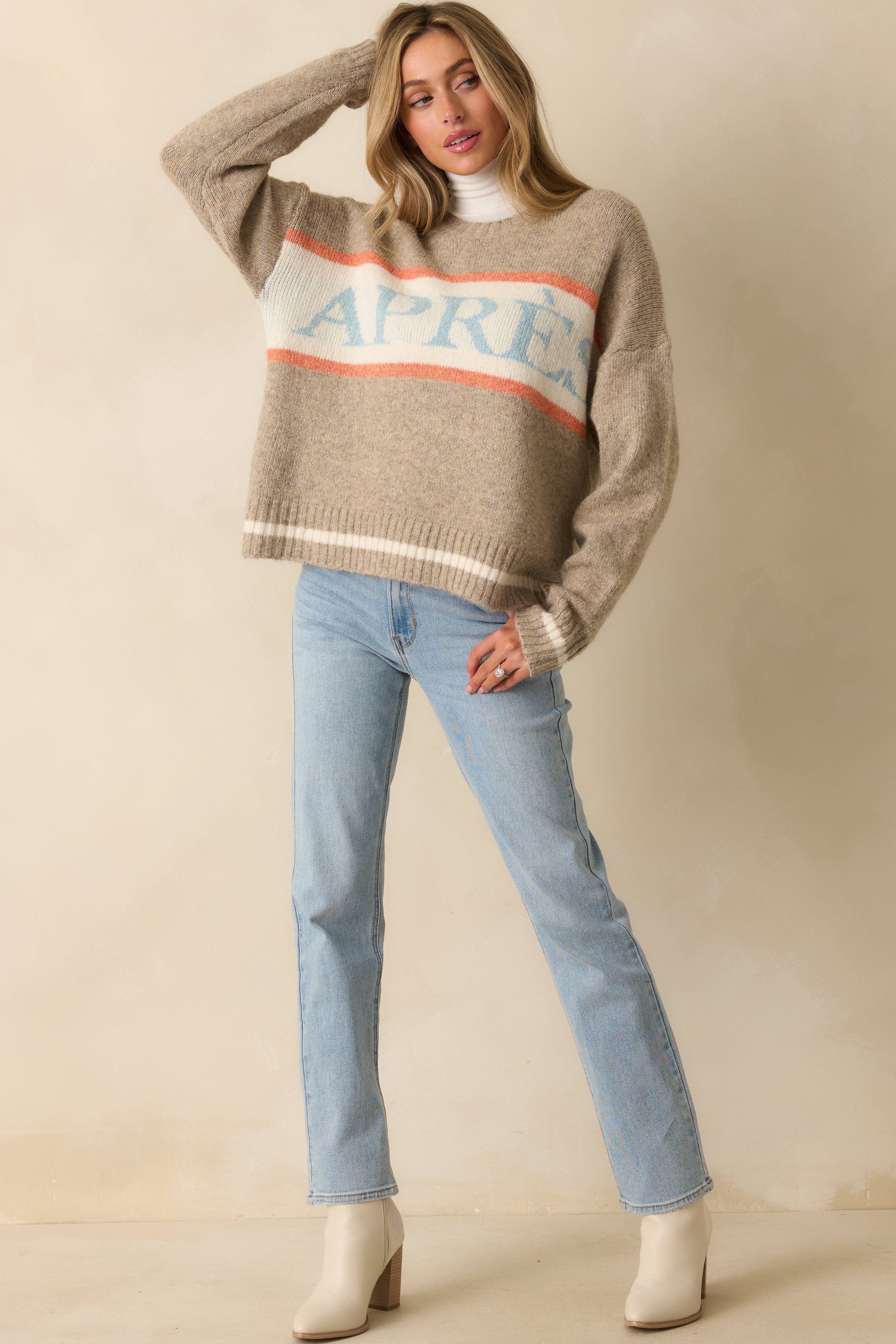 Taupe sweater with relaxed silhouette, orange and ivory stripe accents, and light blue “APRÈS” text.