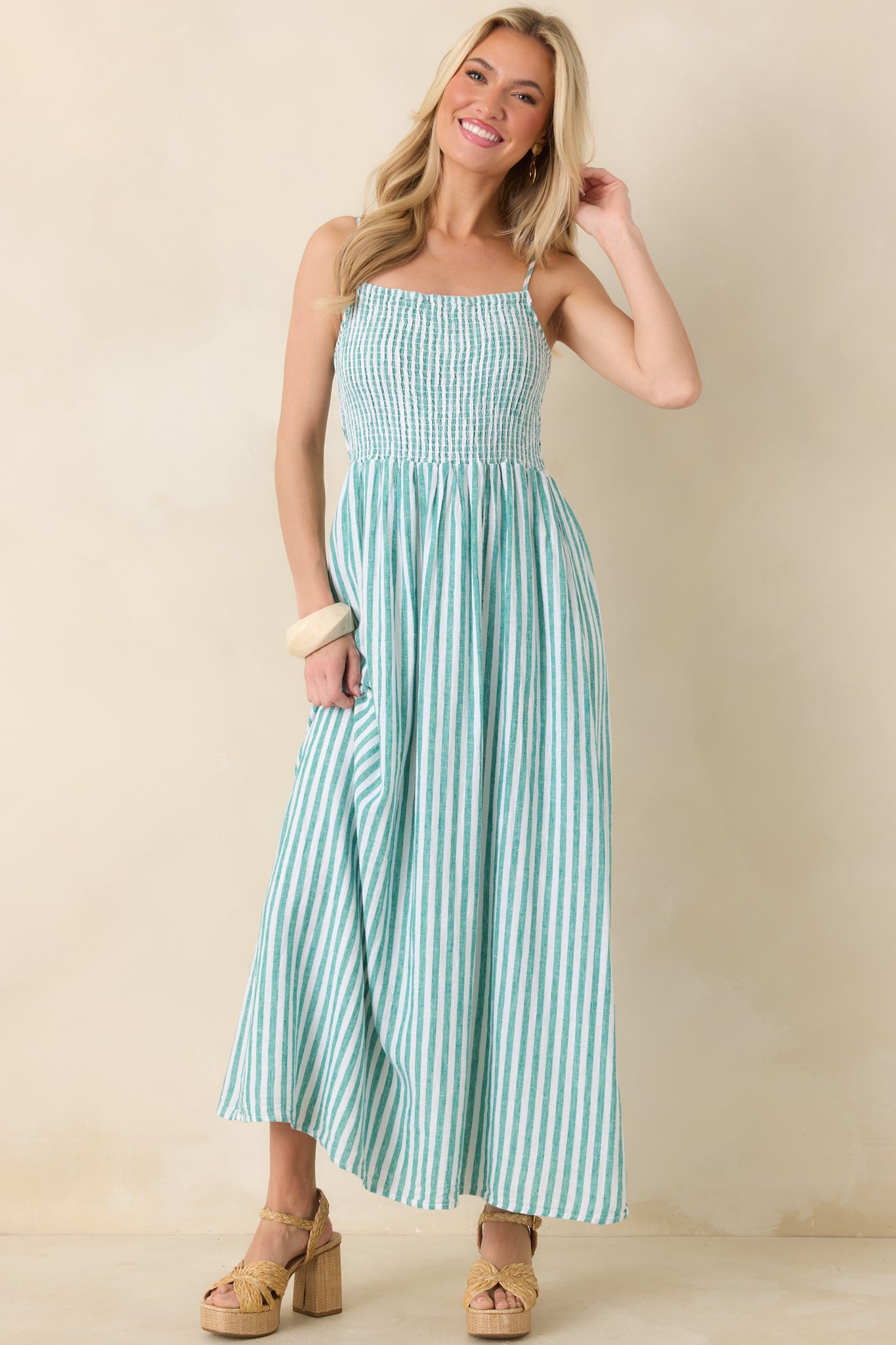 Light teal vertical stripes on a smocked linen maxi dress with adjustable spaghetti straps, shown front on.