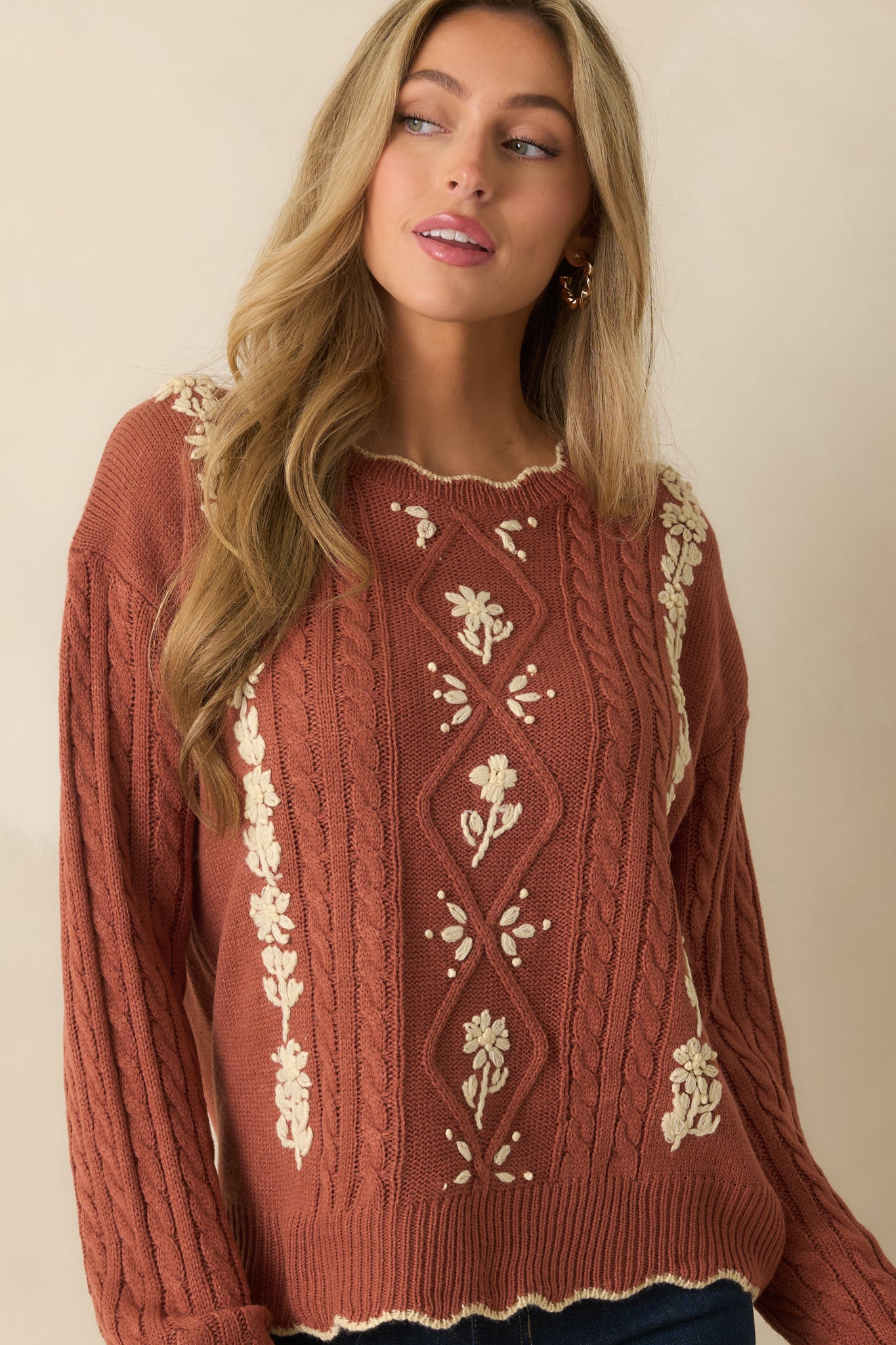 Textured cable knit in terracotta with ribbed cuff and ivory floral embroidery adding contrast.