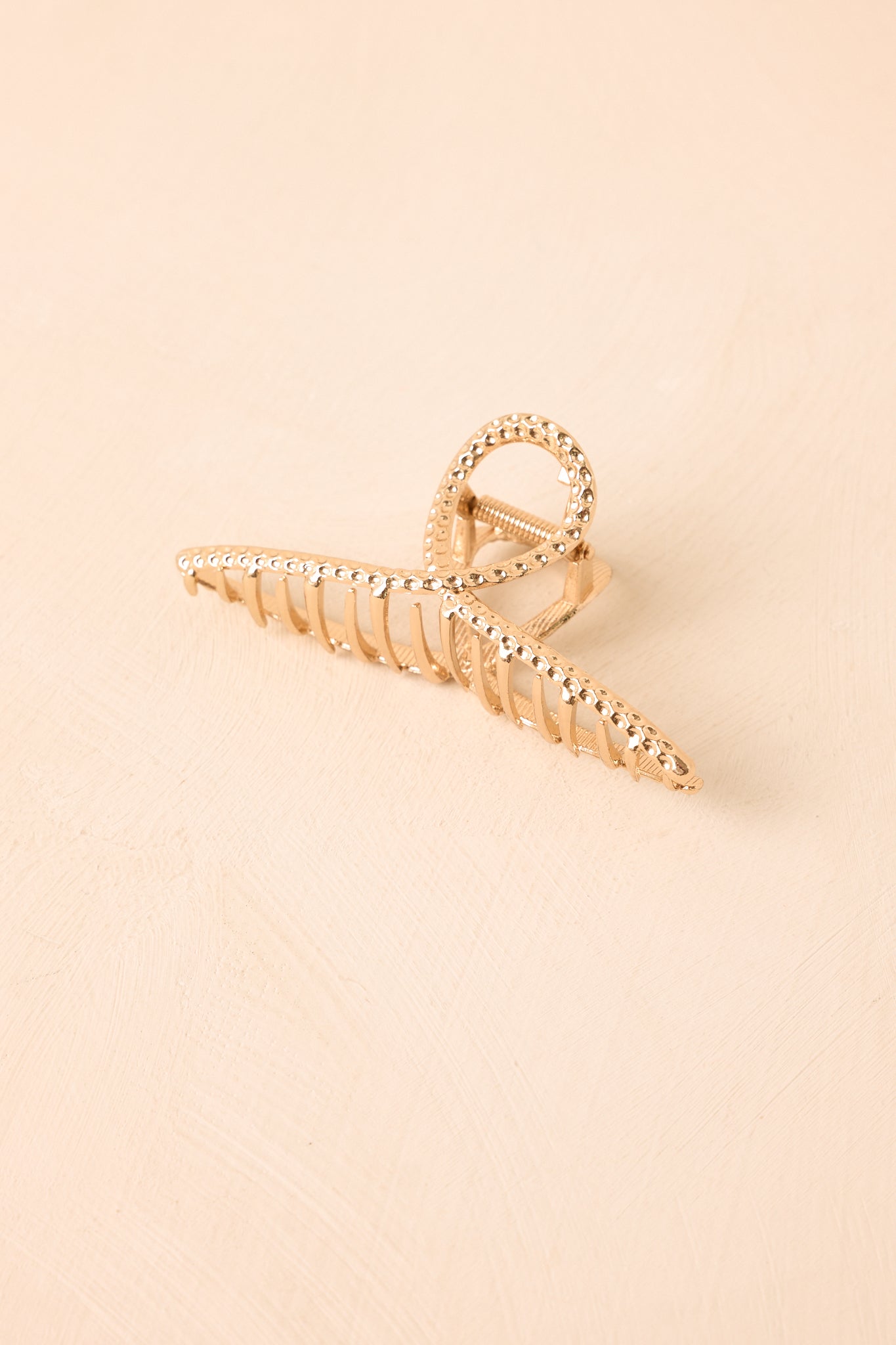 Textured claw hair clip displayed against a beige background featuring an open looping shape, curved silhouette, and secure claw design.