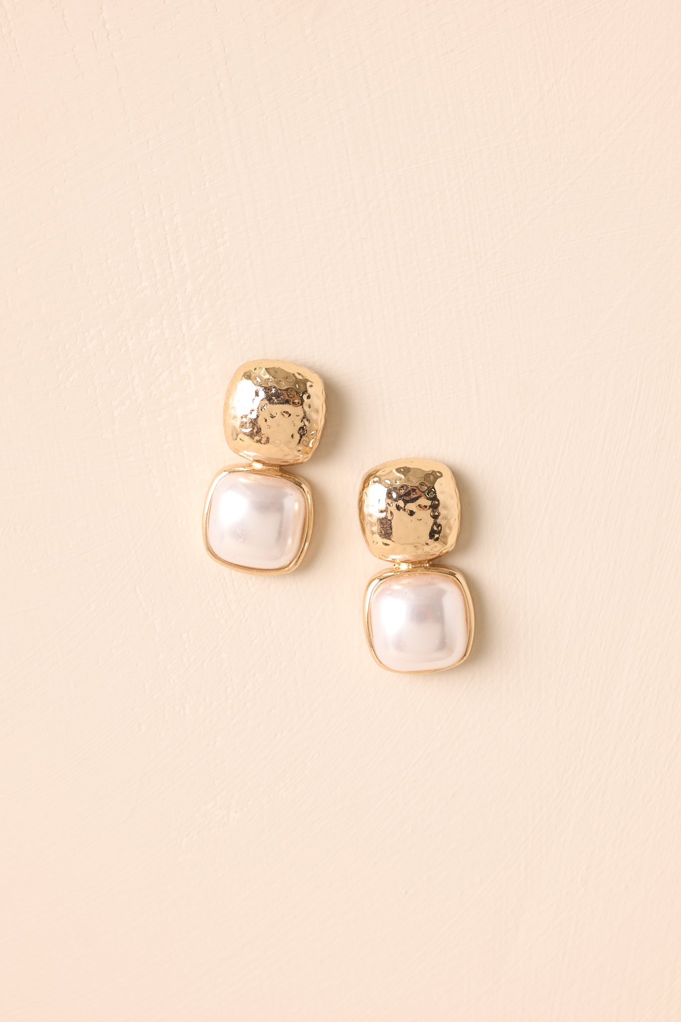Textured gold square earrings with ivory faux pearl accents shown on a neutral beige backdrop.