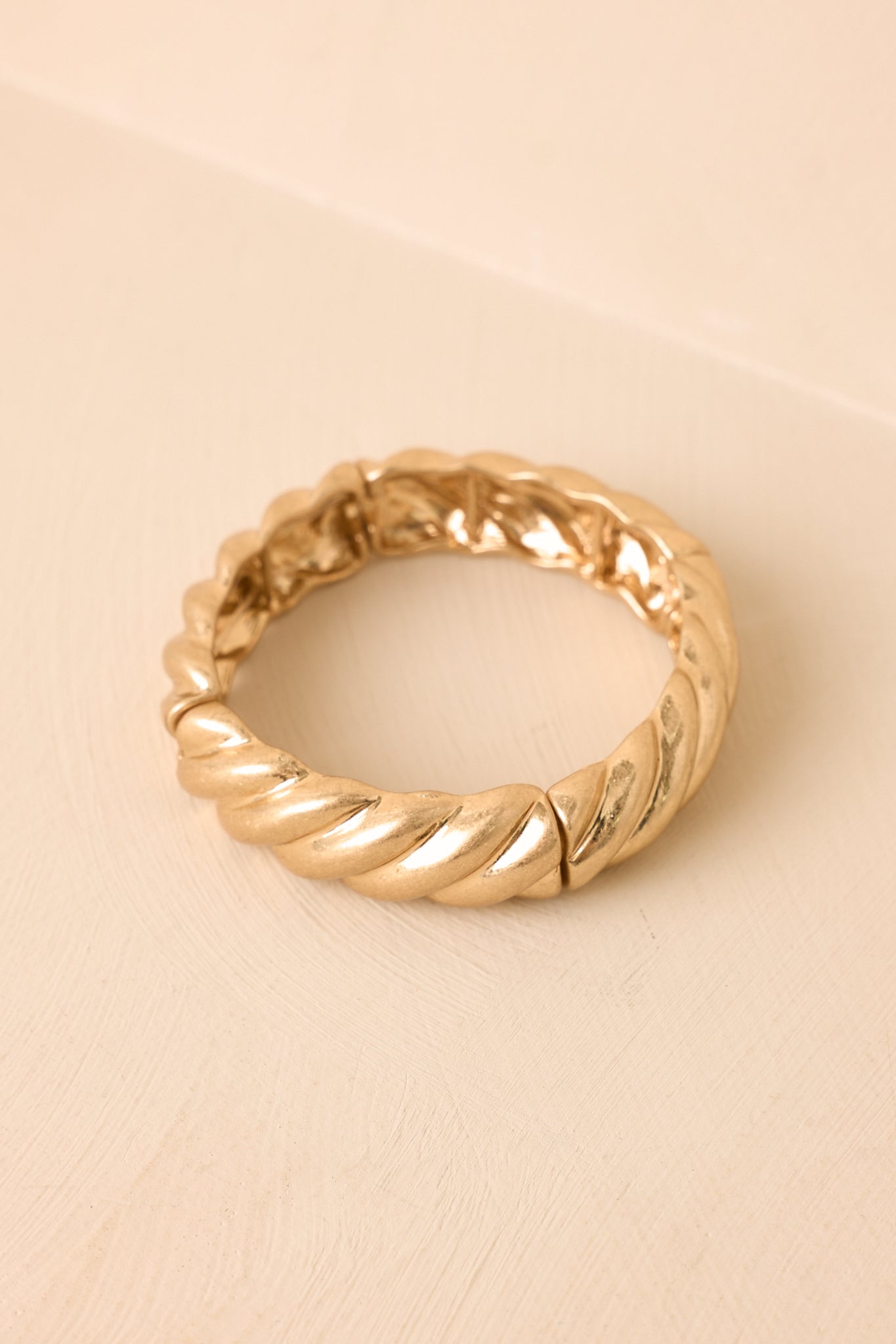 Gold twist bracelet with a textured design on a beige background