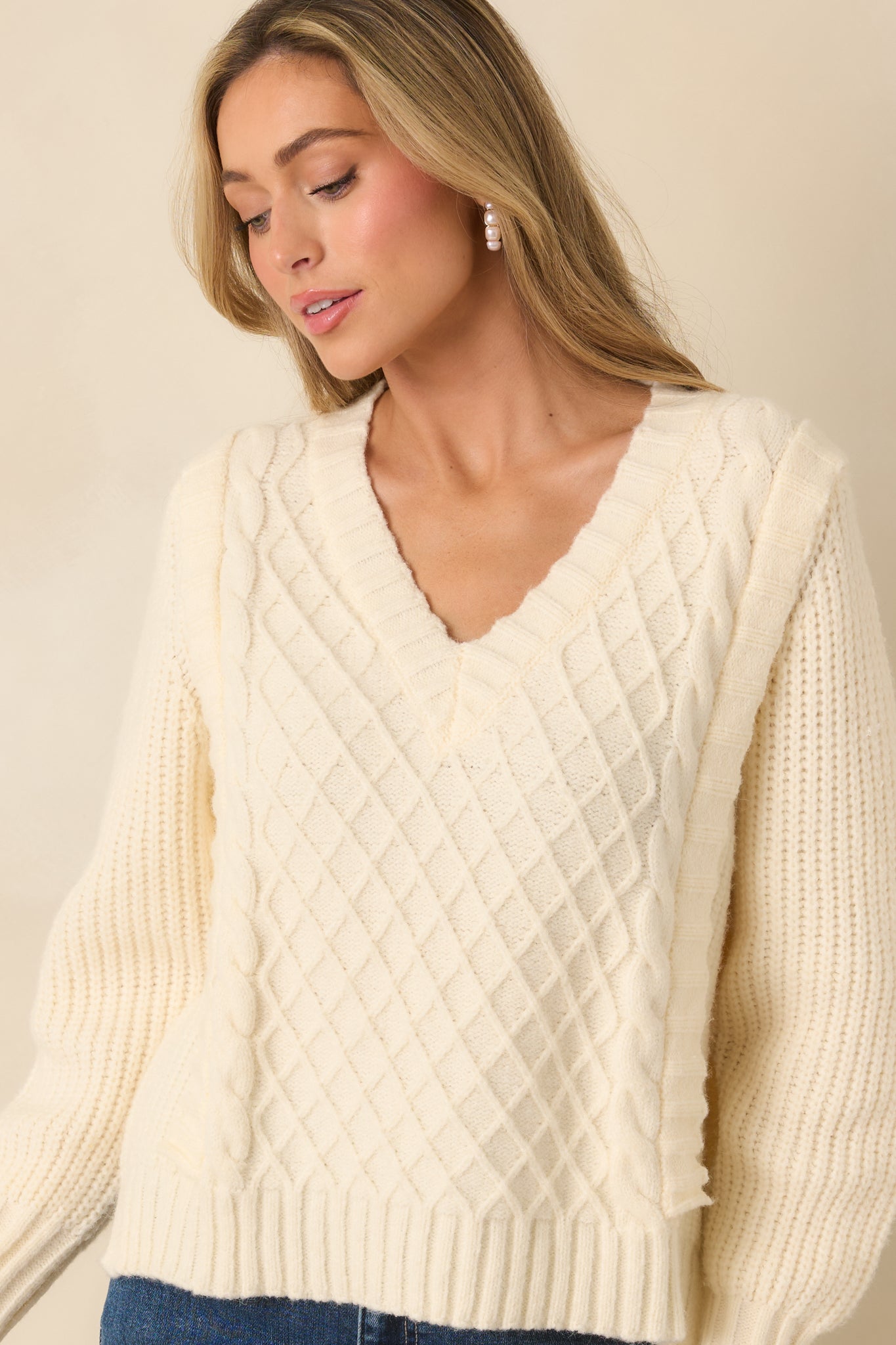 Textured knit paneling on ivory sweater, showing raised stitch design and V-neck shape.