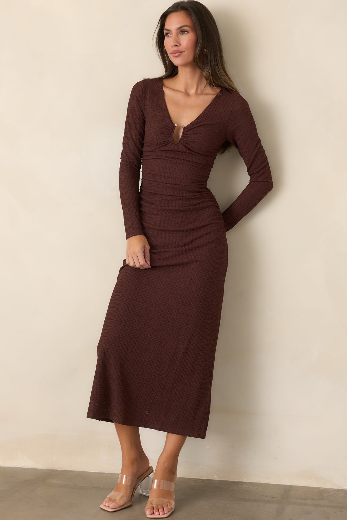 Textured midi dress features a deep V-neckline, front keyhole with metallic hardware, and long sleeves above a flowing skirt.