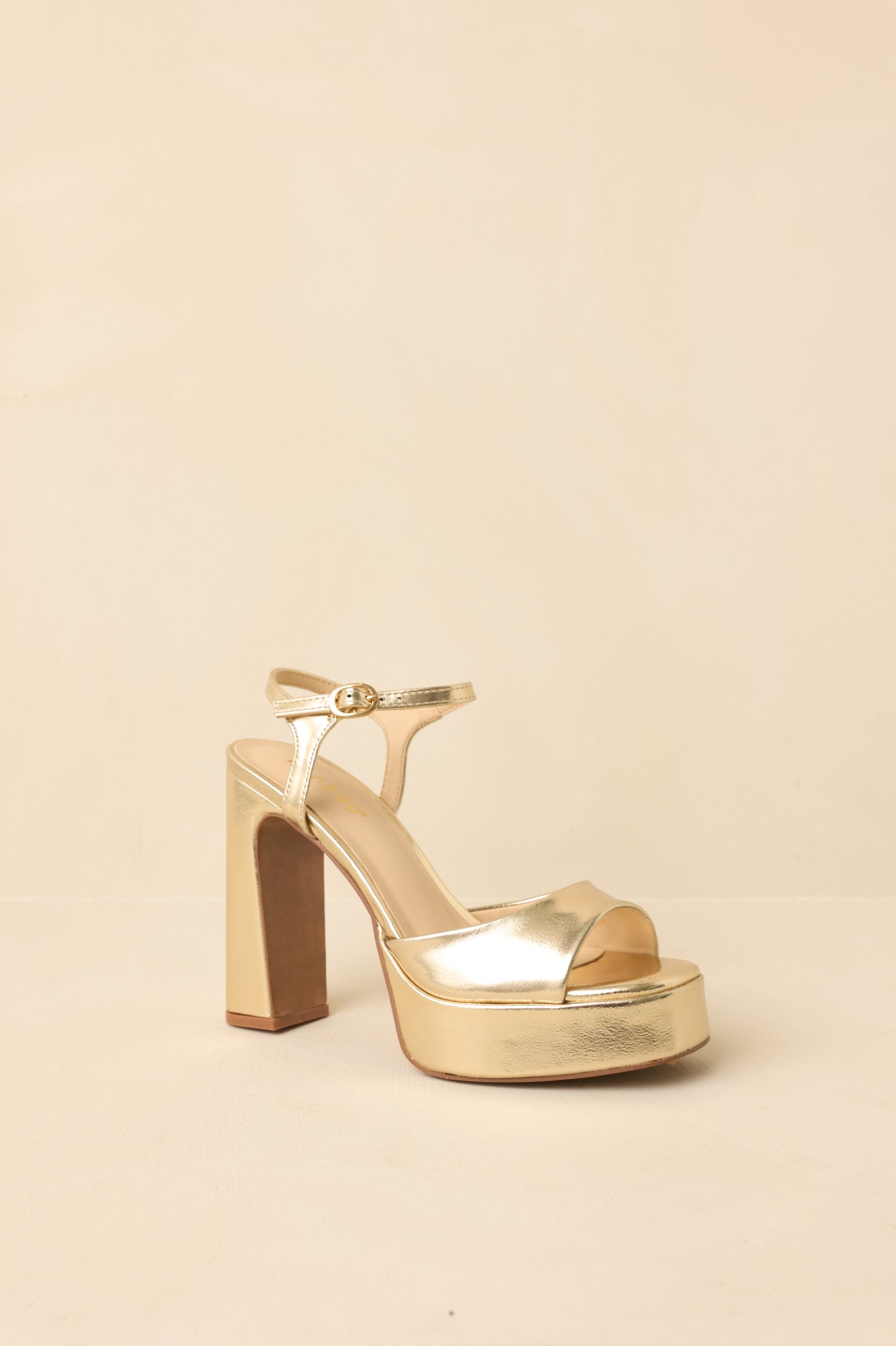 Three-quarter angle of metallic gold platform sandals on beige background emphasizing structured silhouette