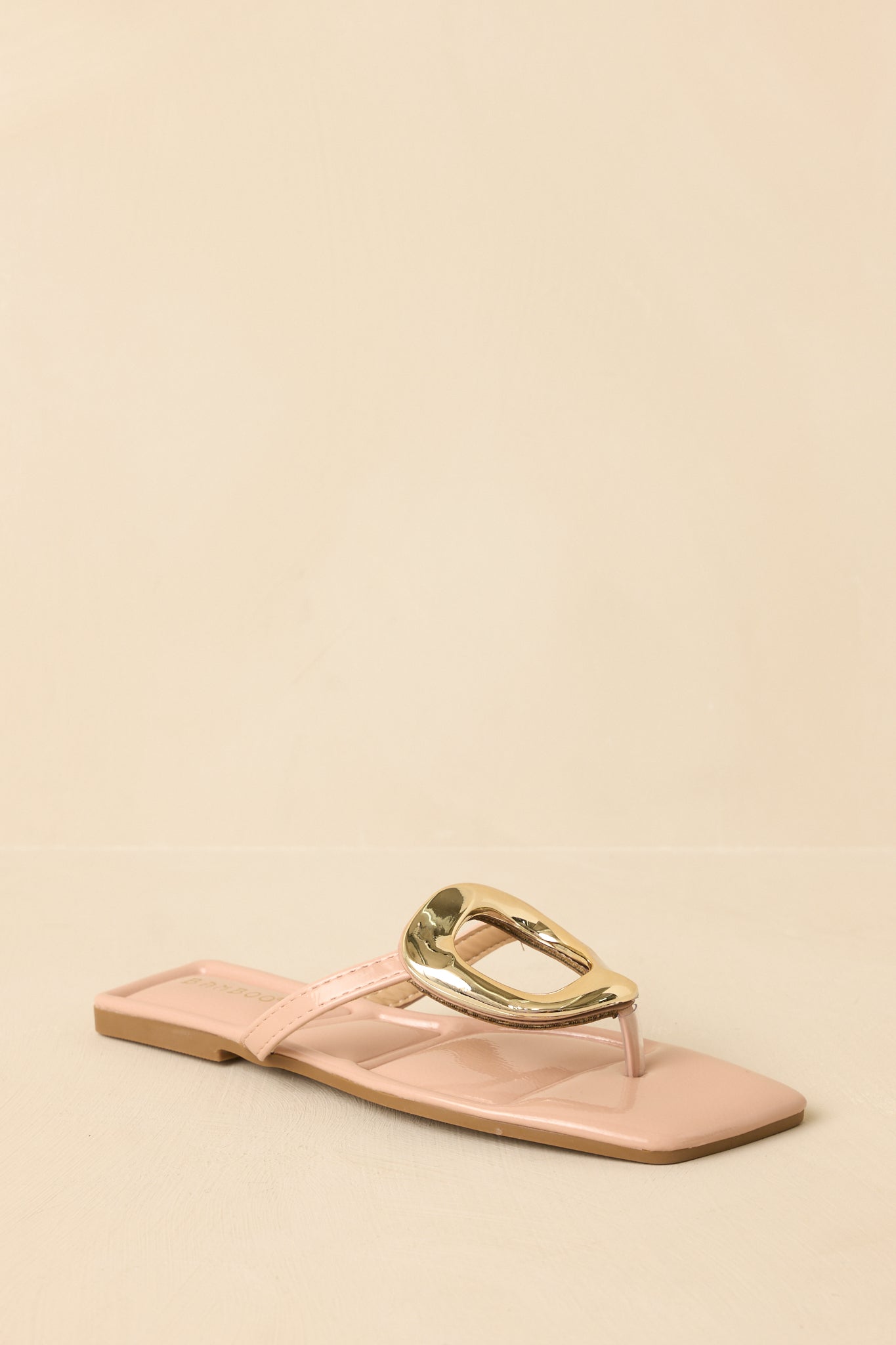 Three-quarter angle view of the nude flat sandals showcasing the glossy finish and thong strap placement.