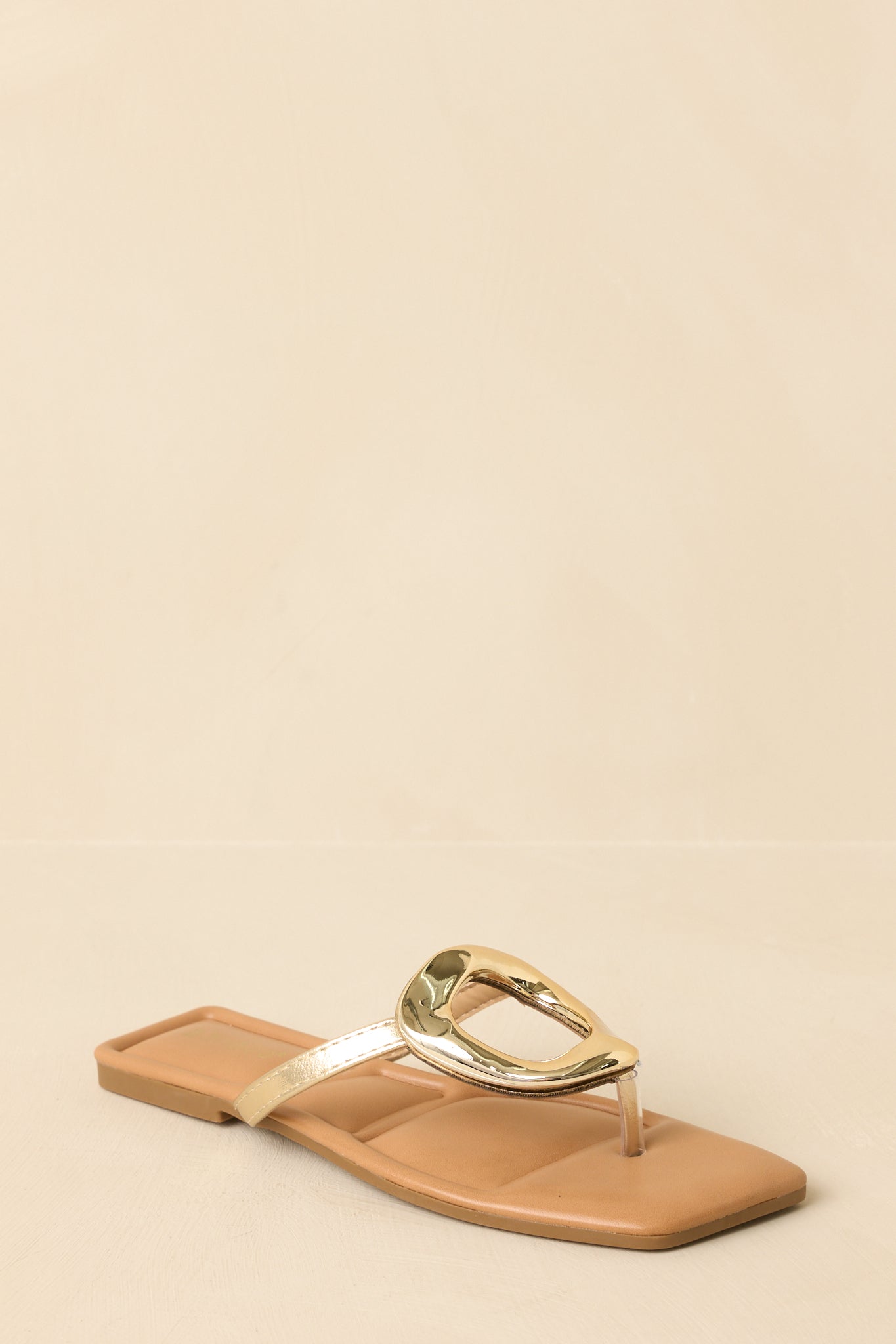 Three-quarter angle view of the gold flat sandals showcasing the metallic sheen and thong strap placement.