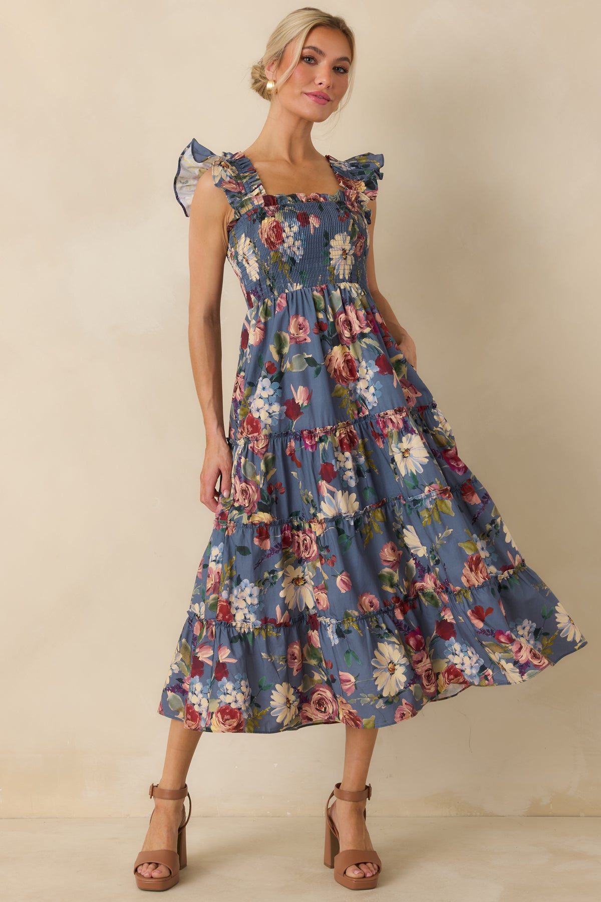 Blue floral midi dress with a fitted smocked top, statement ruffled straps, and gathered tiers creating volume through the skirt.